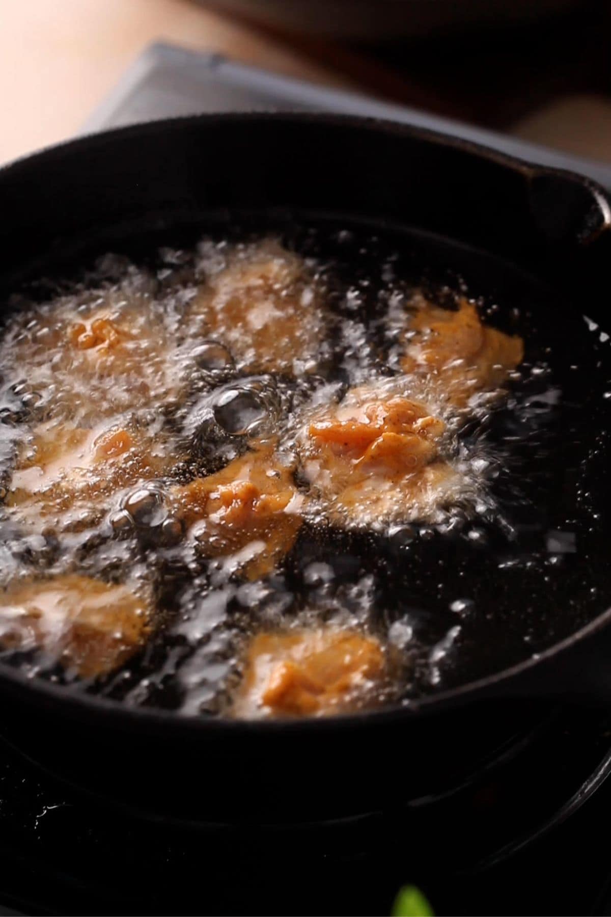 Chicken is deep frying in oil in a cast iron pot.