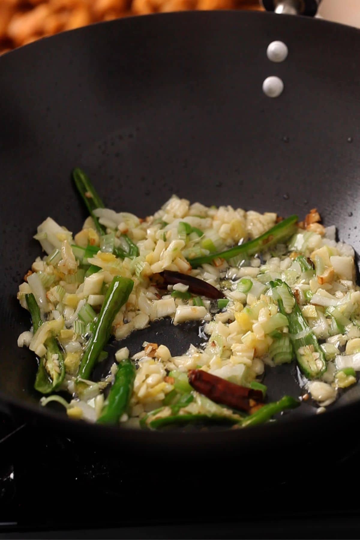 Aromatics and green chillies are stir fried in a black wok. 