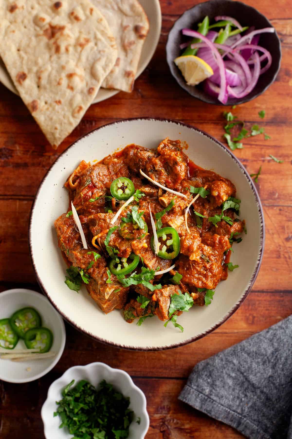 Kadai goat served in a beige bowl and garnished with cilantro and ginger. 