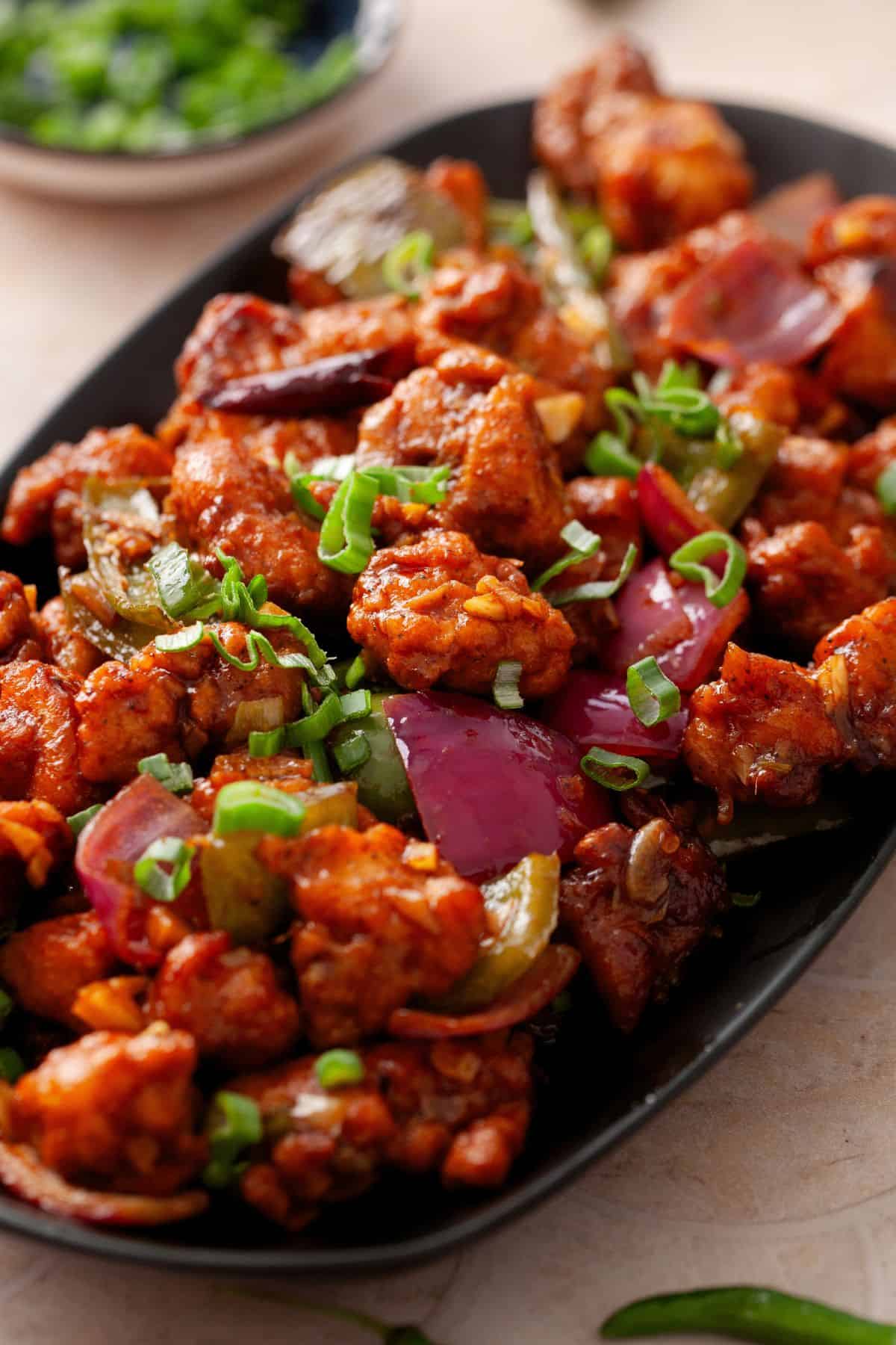 Side image of indo chinese spicy chicken served in a an oval black platter.