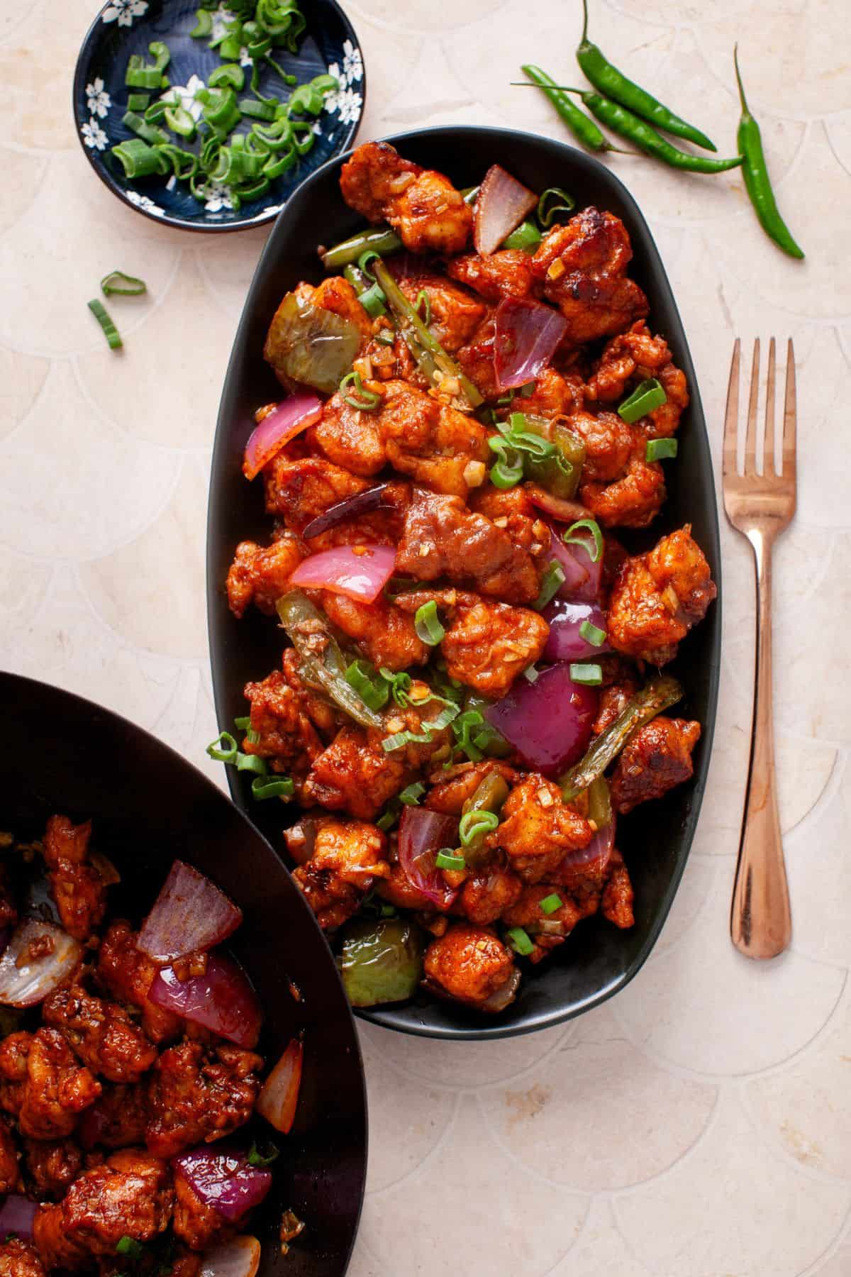 Image of indo chinese spicy chilli chicken served in a an oval black platter.