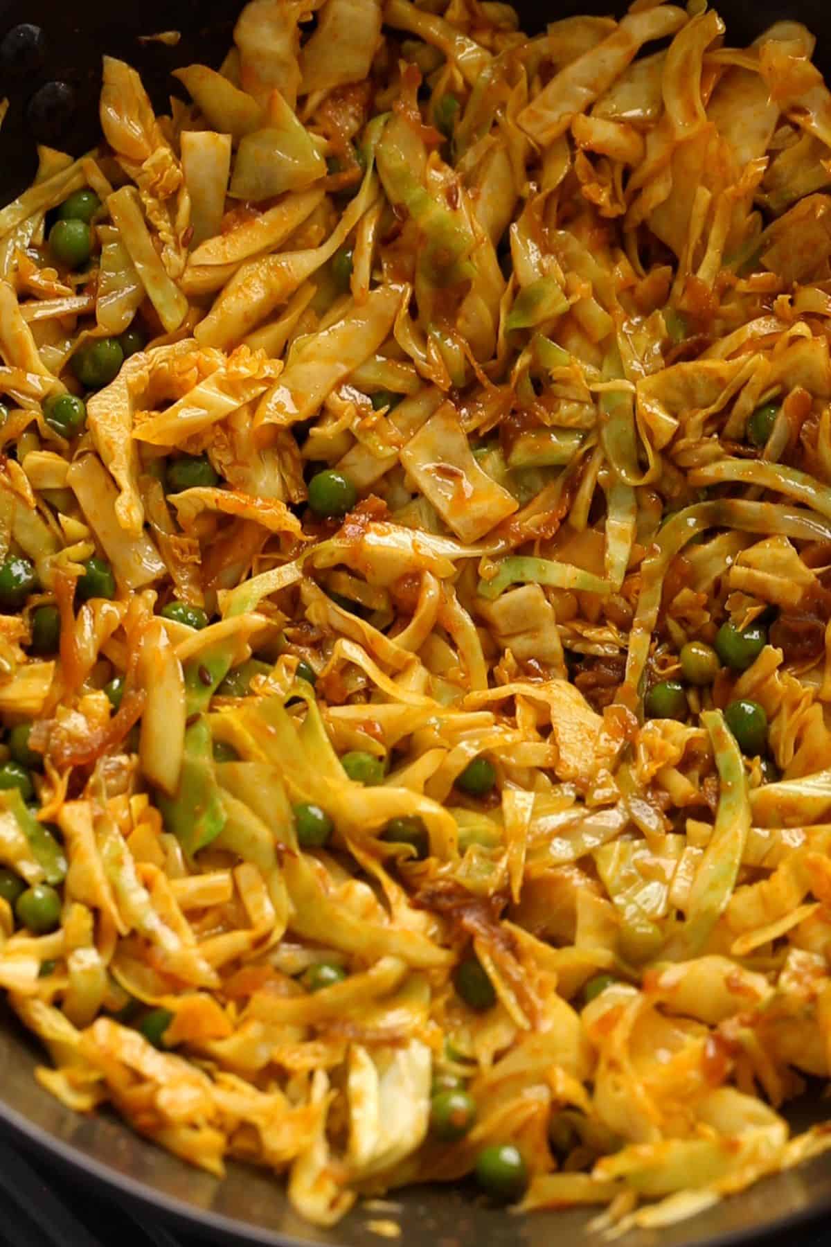 A close-up of cooked cabbage and peas, seasoned with spices.