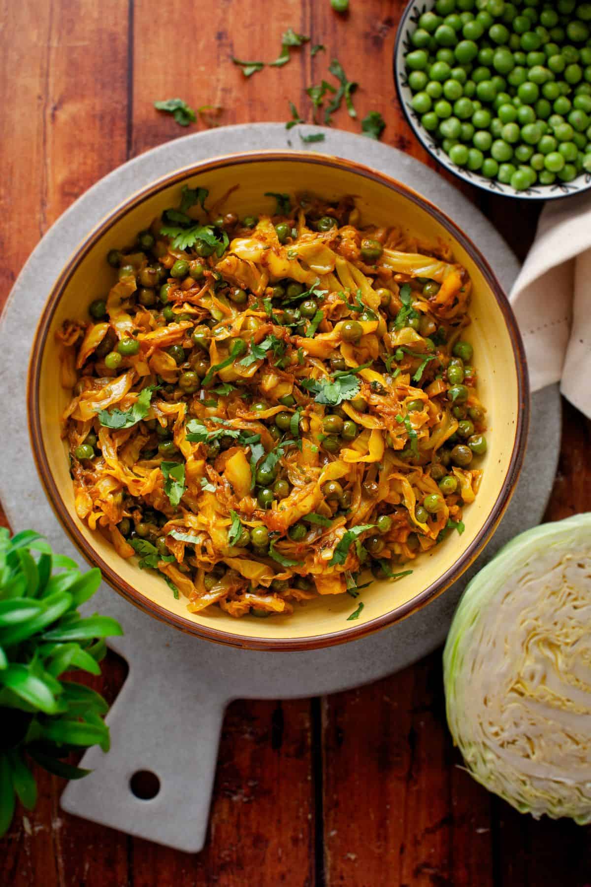 A bowl of cabbage sabzi garnished with fresh cilantro, placed on a round gray plate on a wooden table.