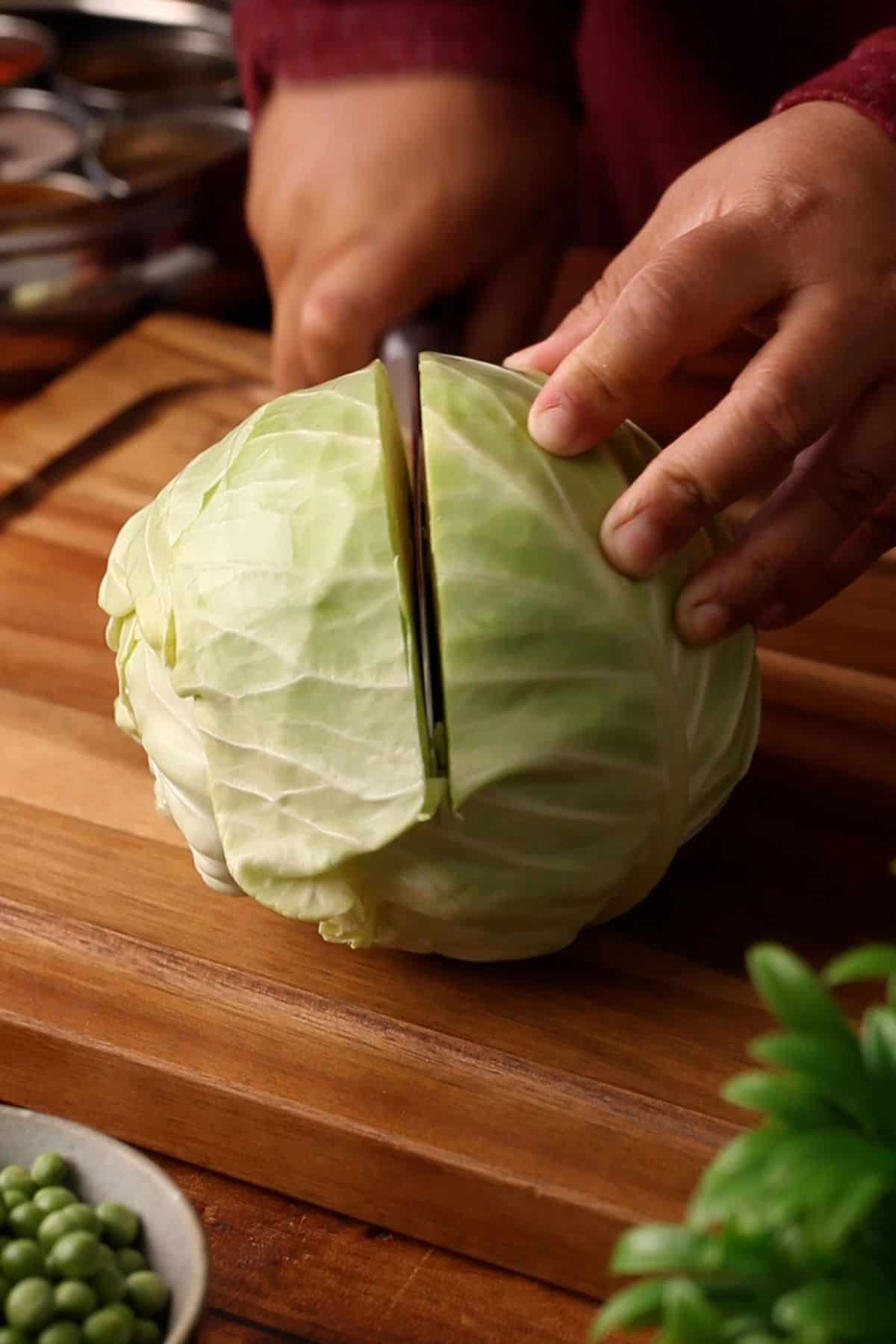 Cutting a small cabbage into half on a wooden chopping board.