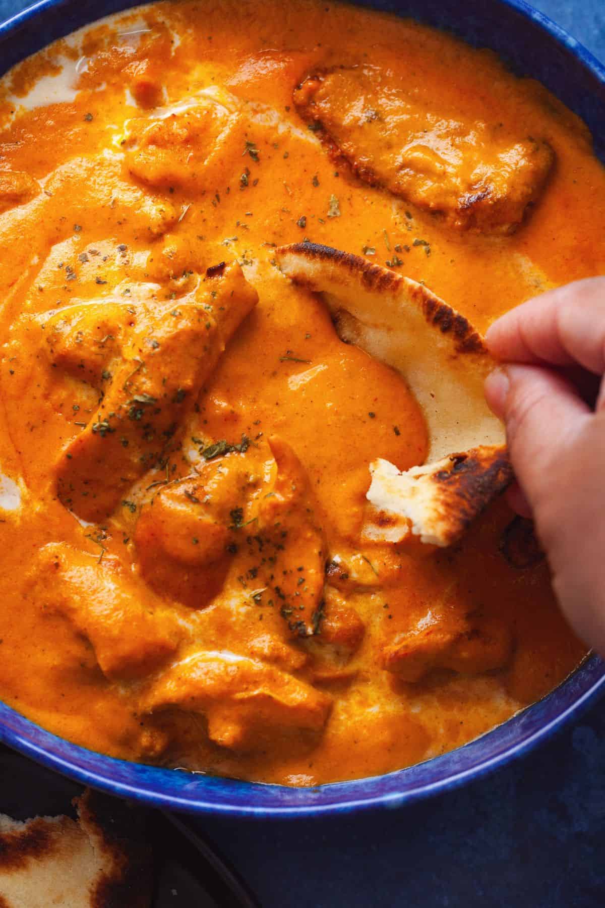 Image of dipping  a piece of naan into a bowl of creamy butter chicken. 