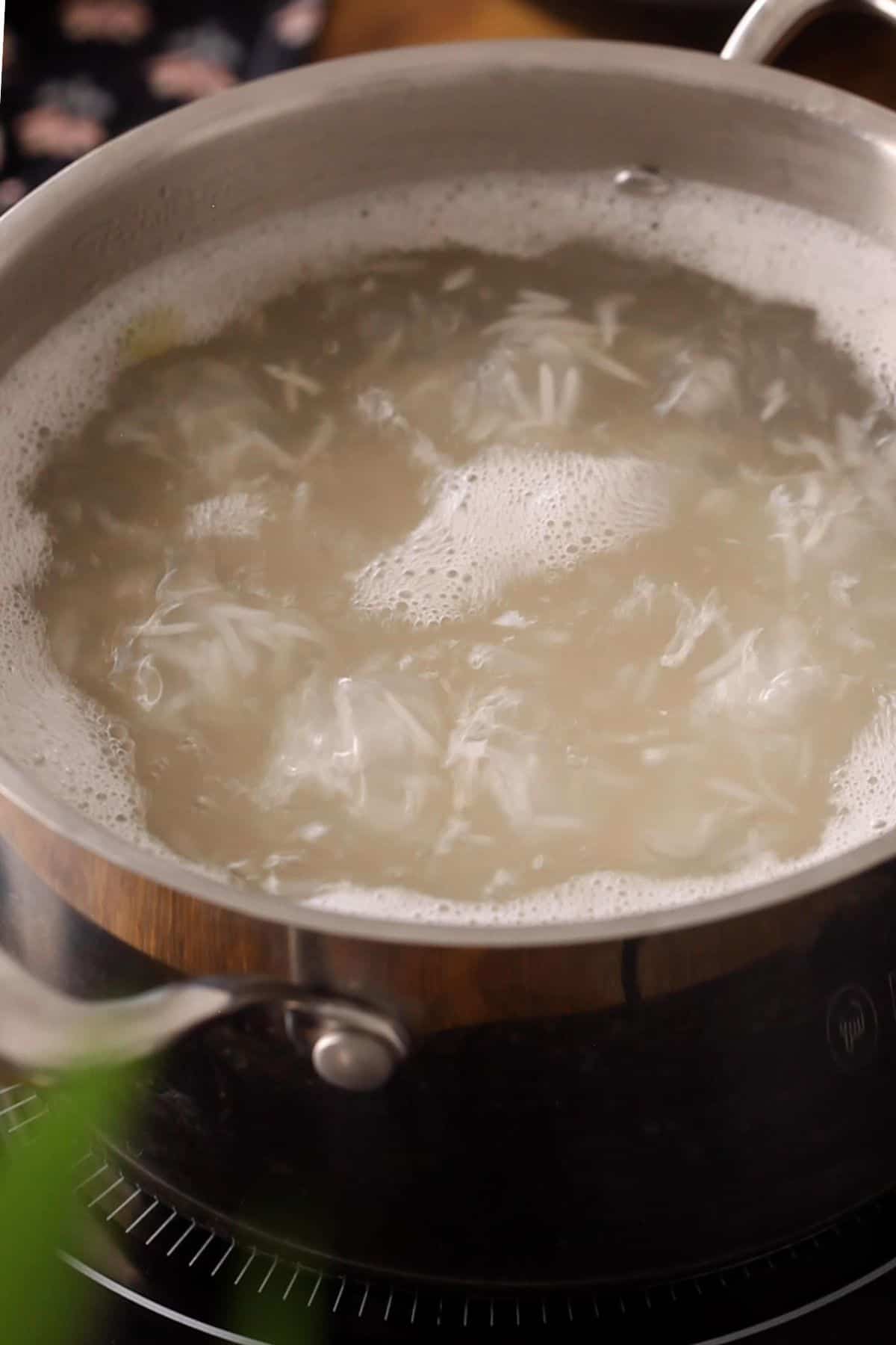 Basmati rice is boiling with spices in a steel pot.