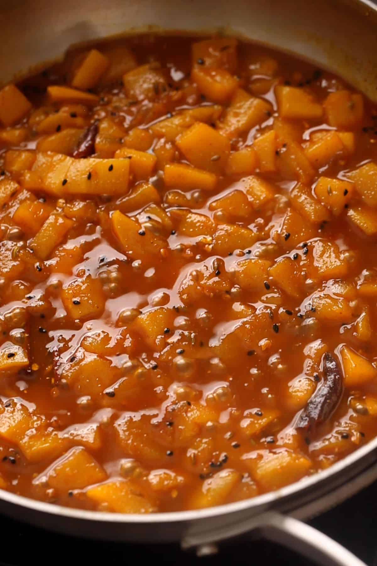 A pan filled with cooked diced mangoes in a thick, reddish-brown syrup.