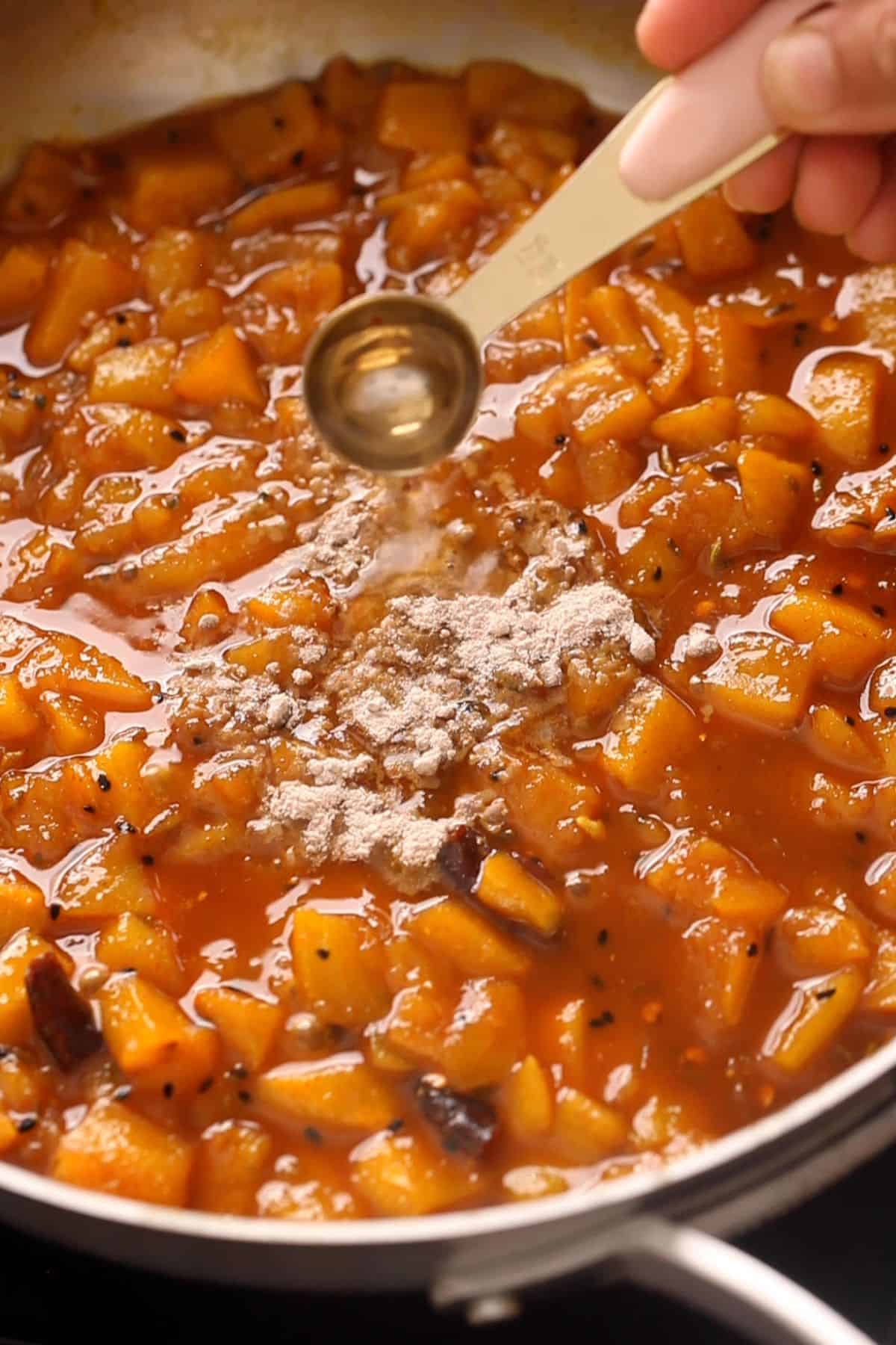 Adding black salt and vinegar to cooked mango chutney.