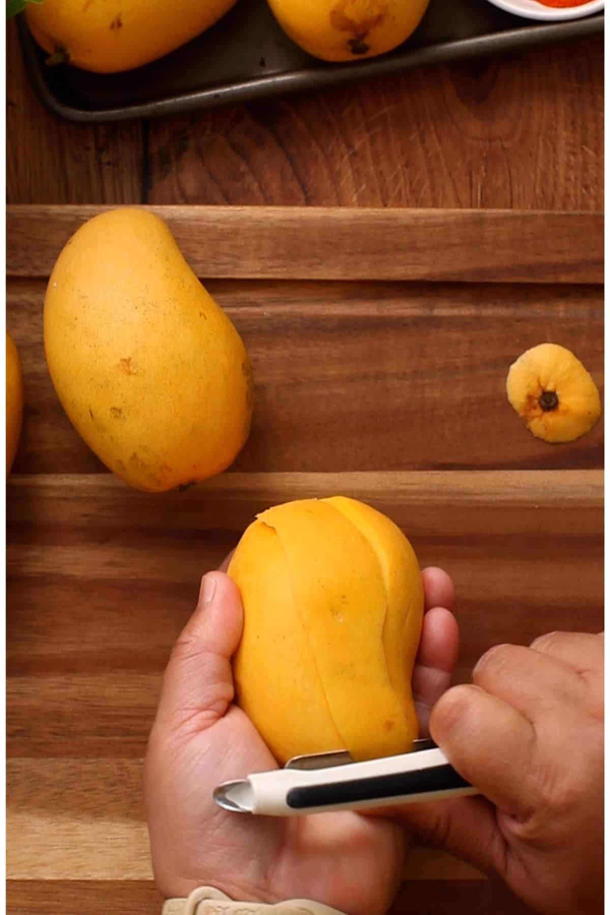 Peeling honey mangoes using a white & black peeler.