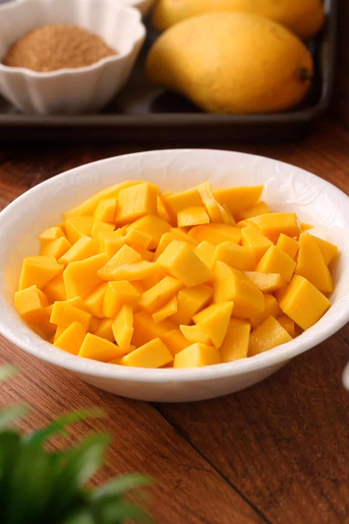 Diced mangoes in a white bowl placed on a wooden bowl.