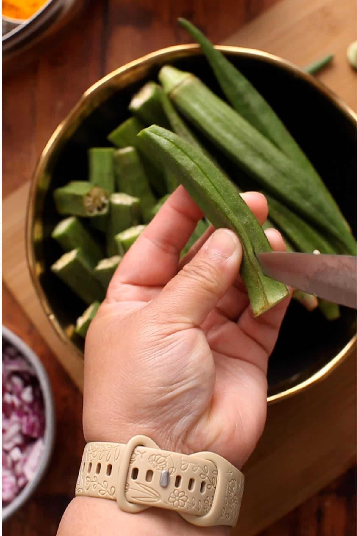 Slitting fresh bhindi in the center using a small knife.