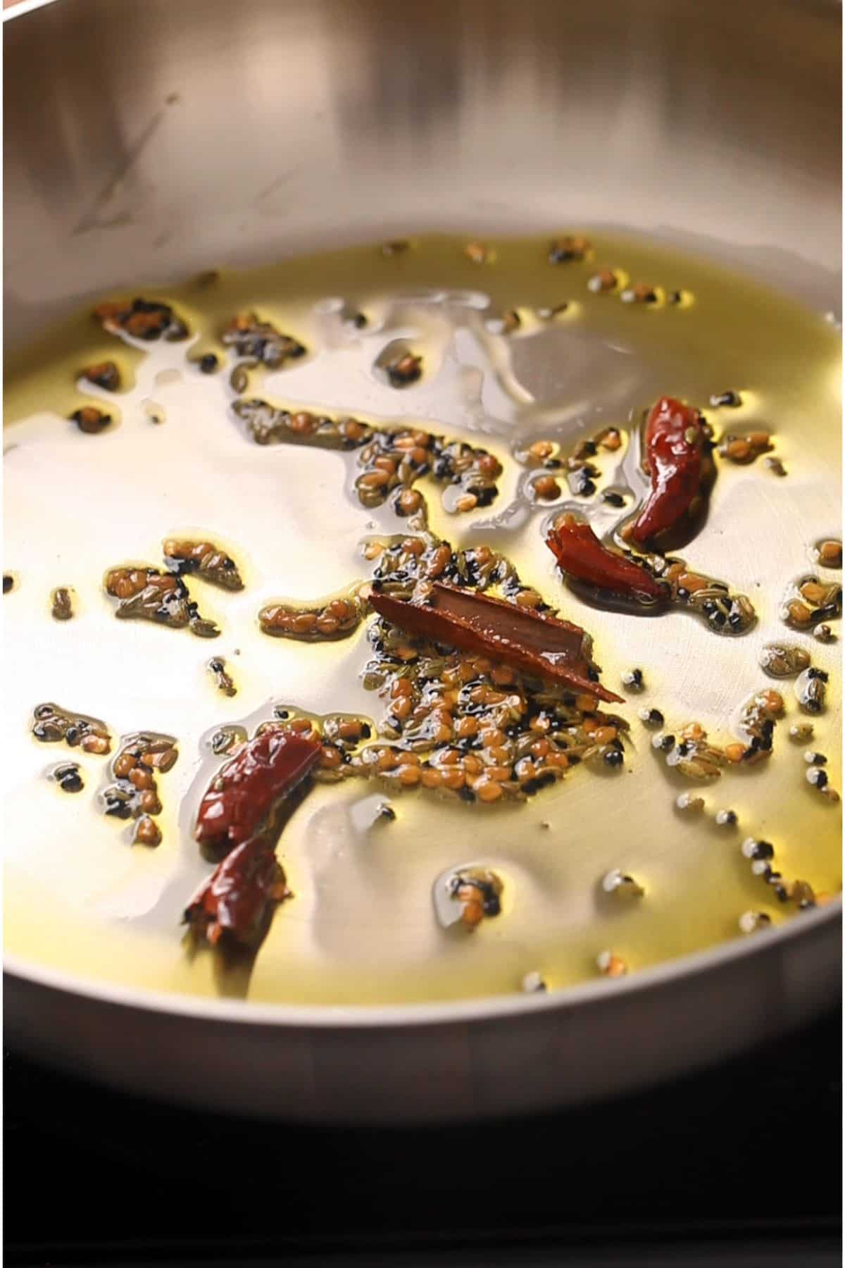 Whole spices and dried red chilli tempered in mustard oil in a steel pan.