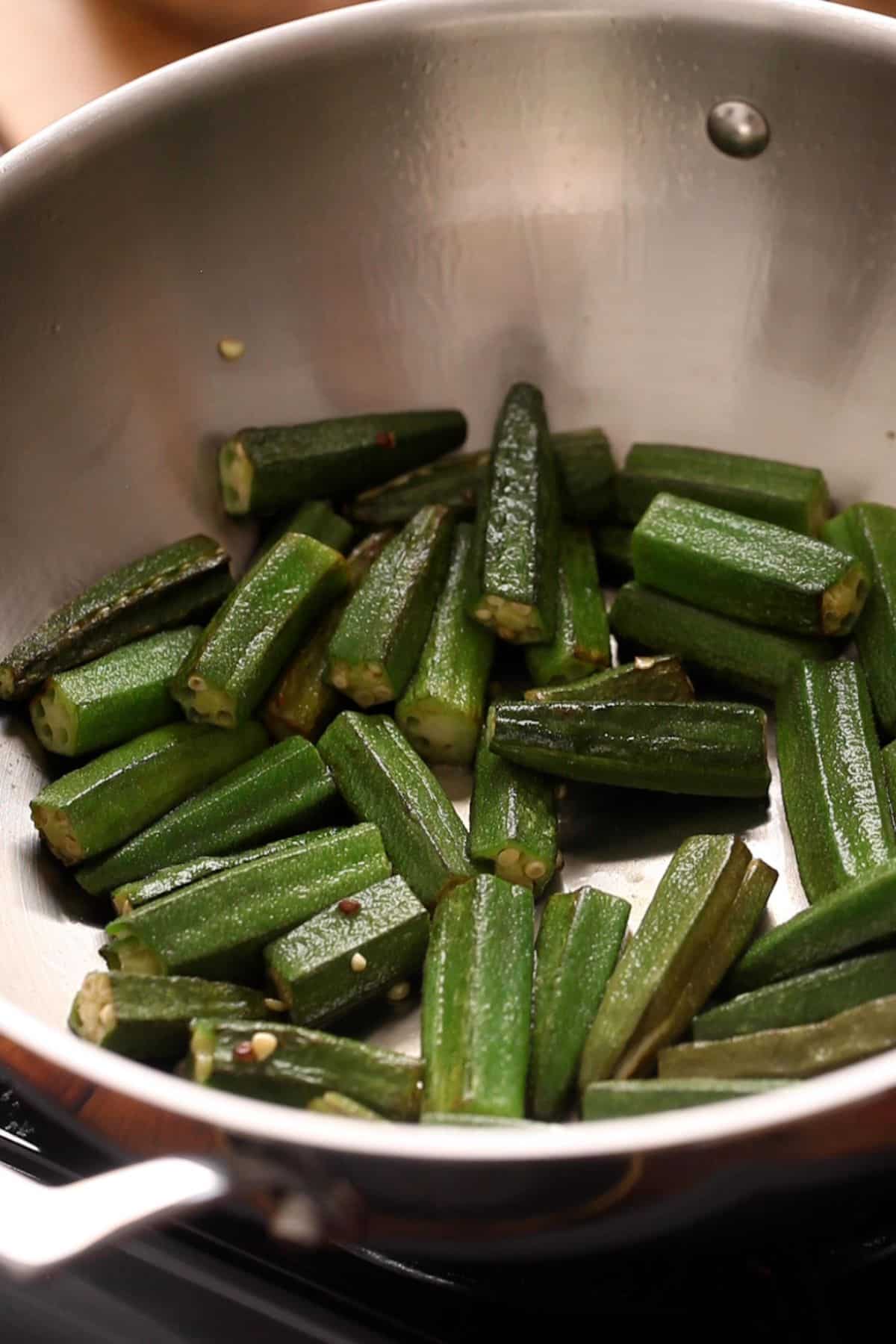 Frying bhindi in oil in a stainless steel wok.