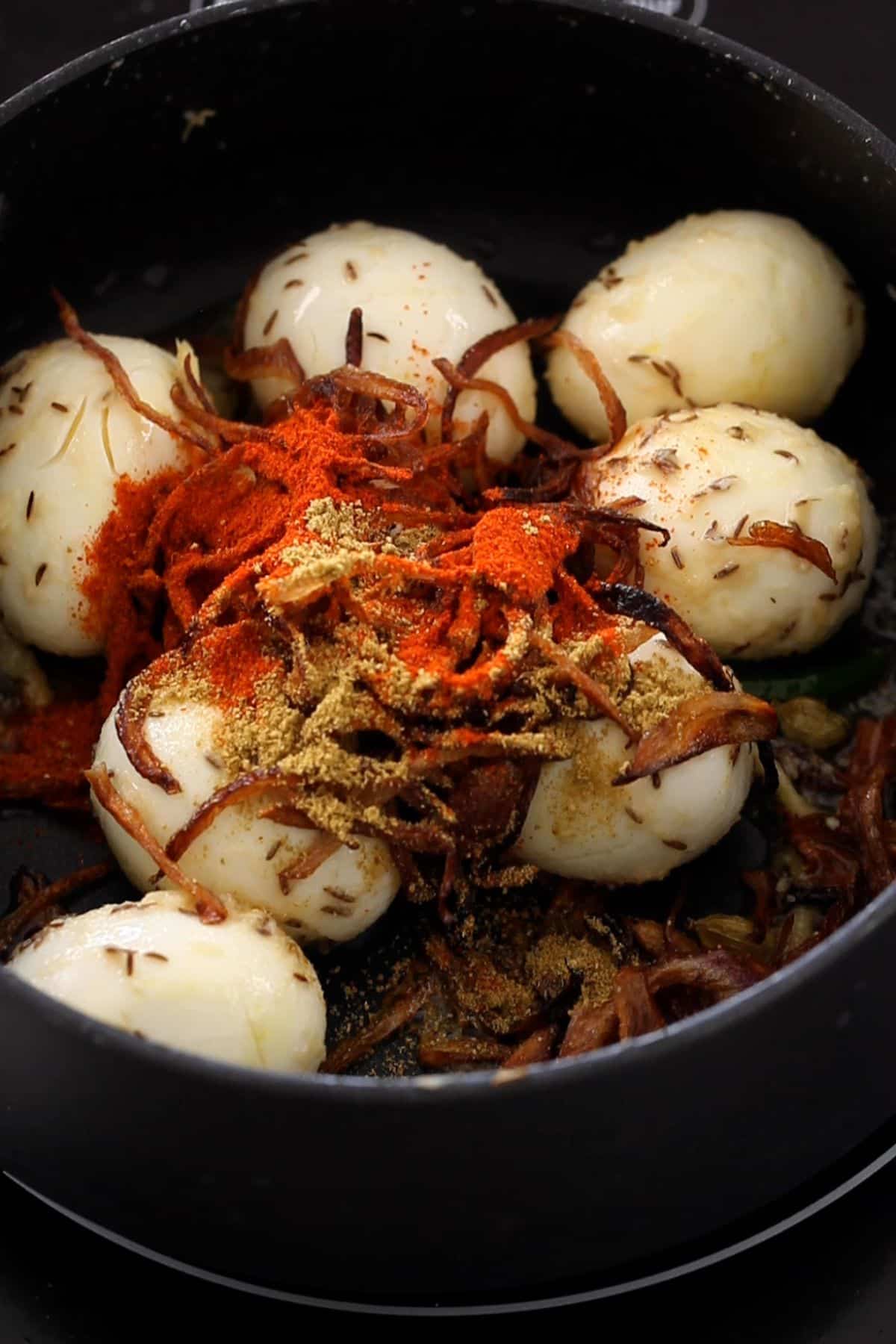Eggs in a black cooking pot topped with fried onions and sprinkled with  spices.