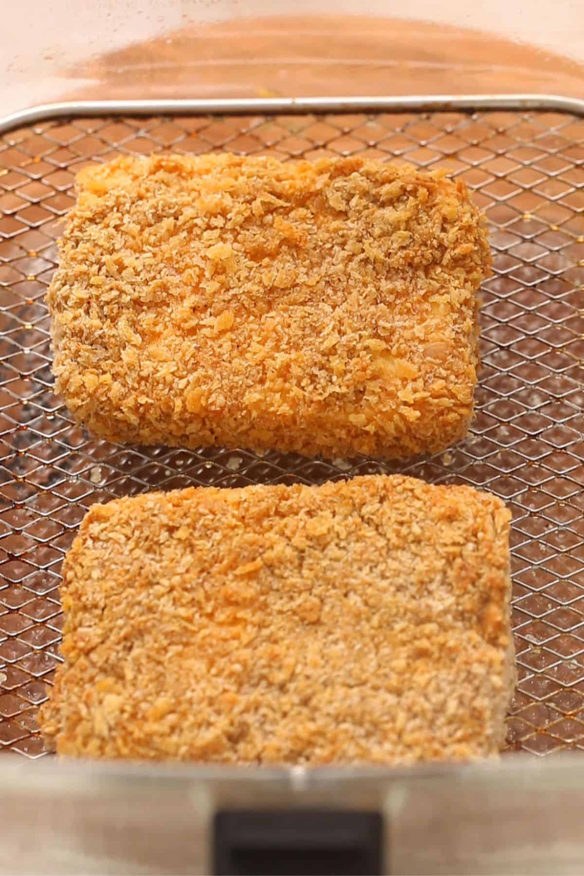 Golden and crispy paneer pieces after air frying placed on a wire basket.