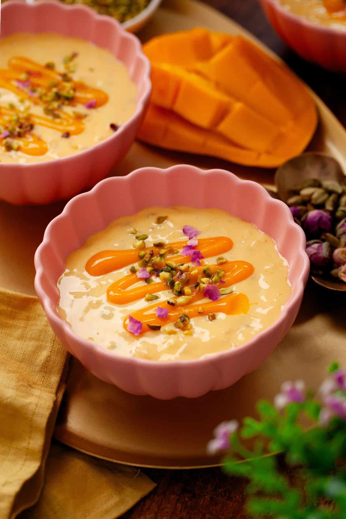 Mango Kheer served in a fluted pink bowl with cut up mango in background.