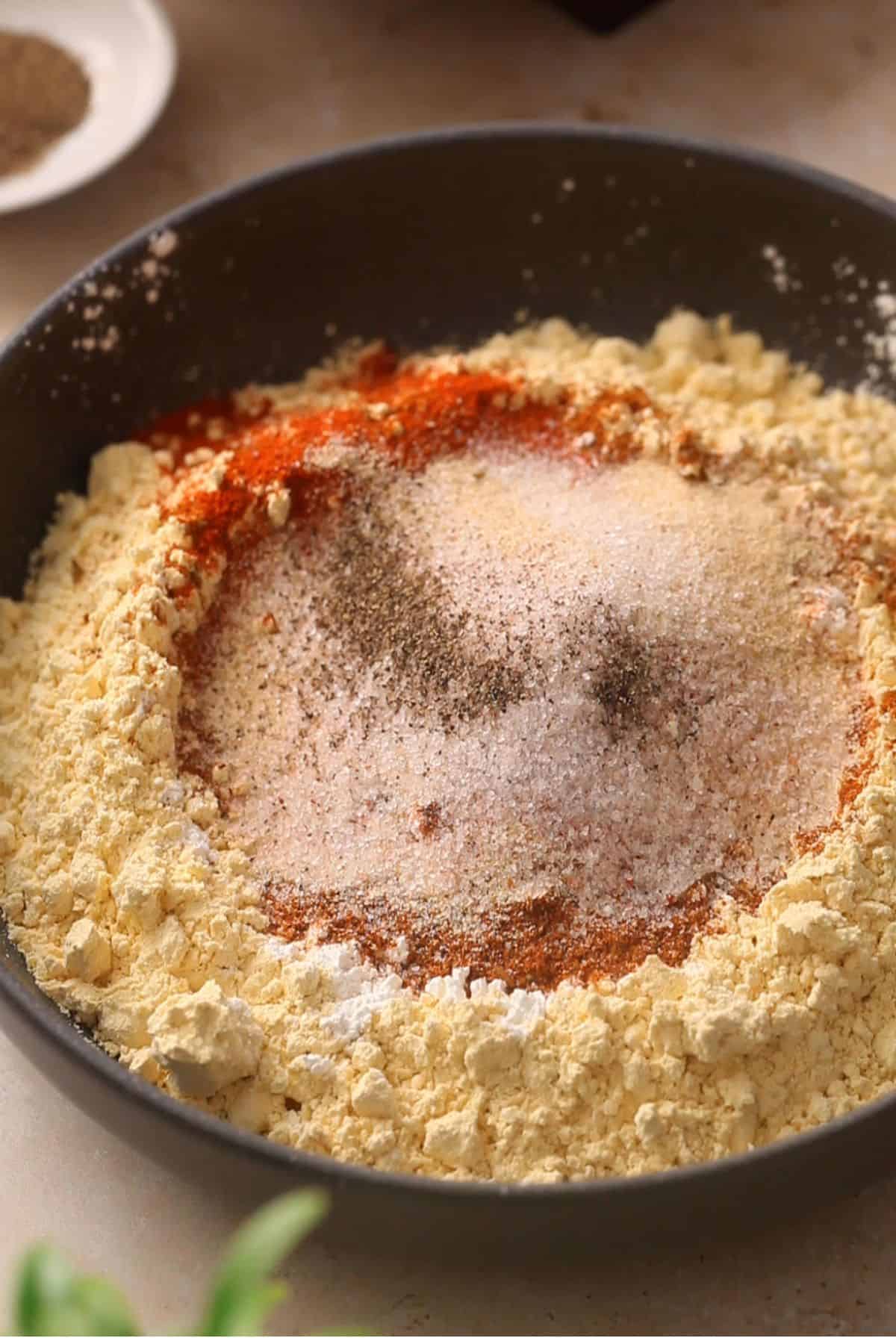 Gram flour mixed with spices and salt in a shallow black bowl.