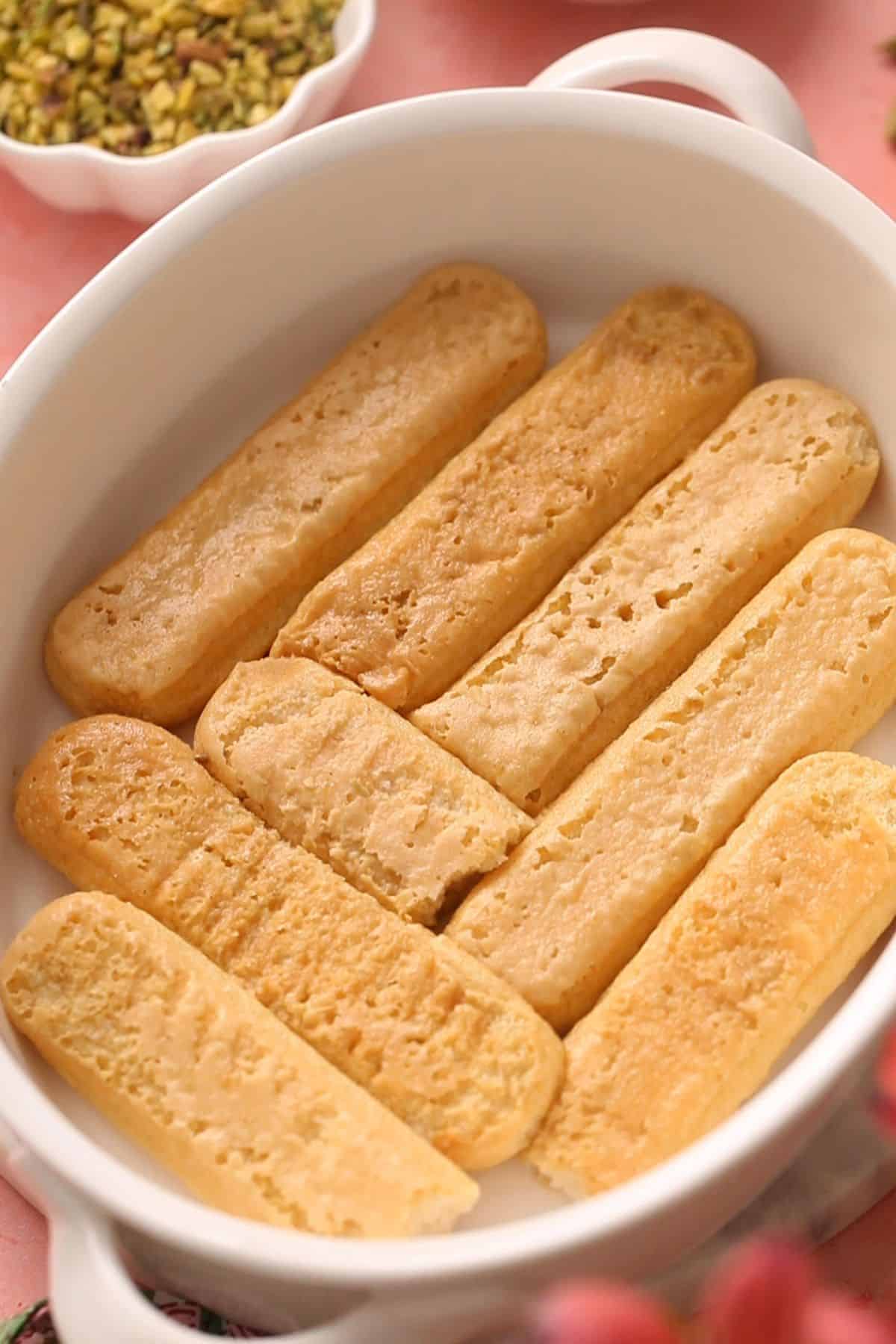 Eight ladyfinger biscuits are neatly arranged in a white oval dish.