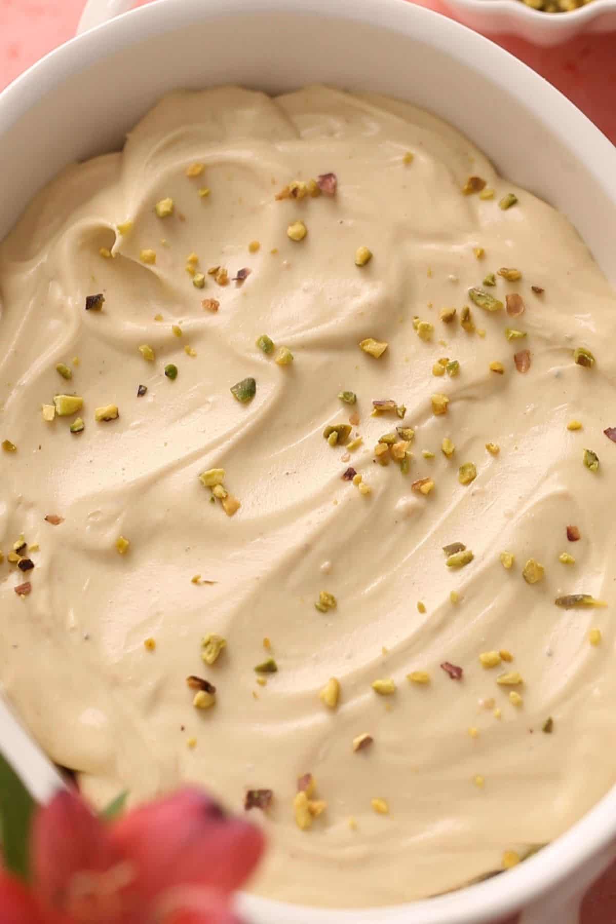 A mixture of cream and rushed pistachios is spread over tiramisu.