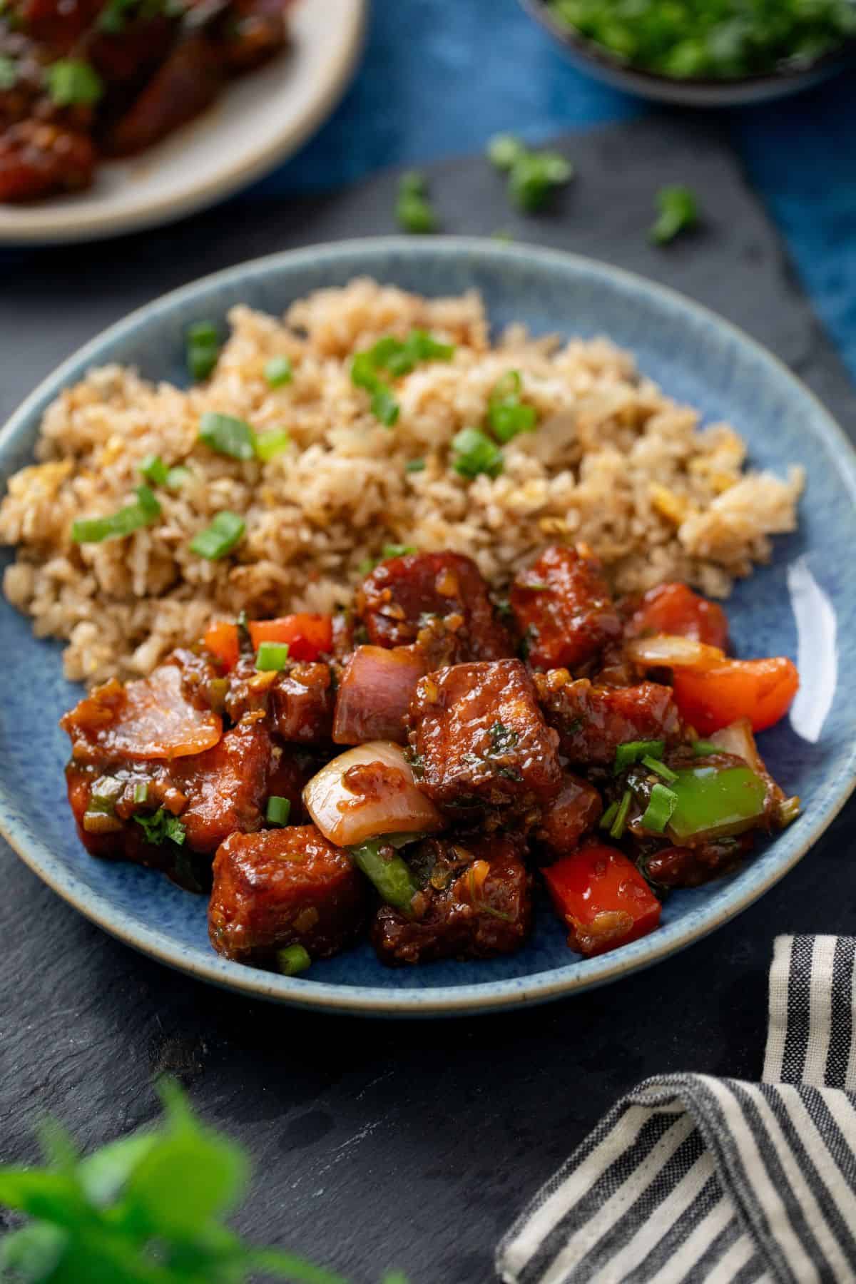 Spicy chili paneer served with fried rice on a blue stone plate.