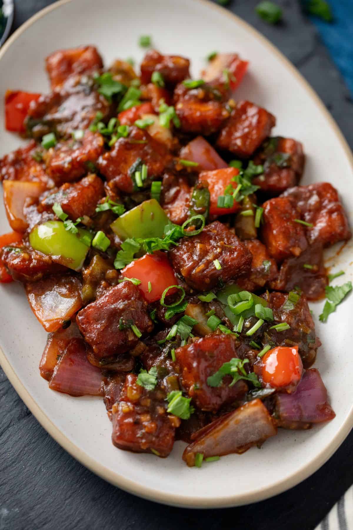 Close up of chilli paneer dish in a abeige oval plate.