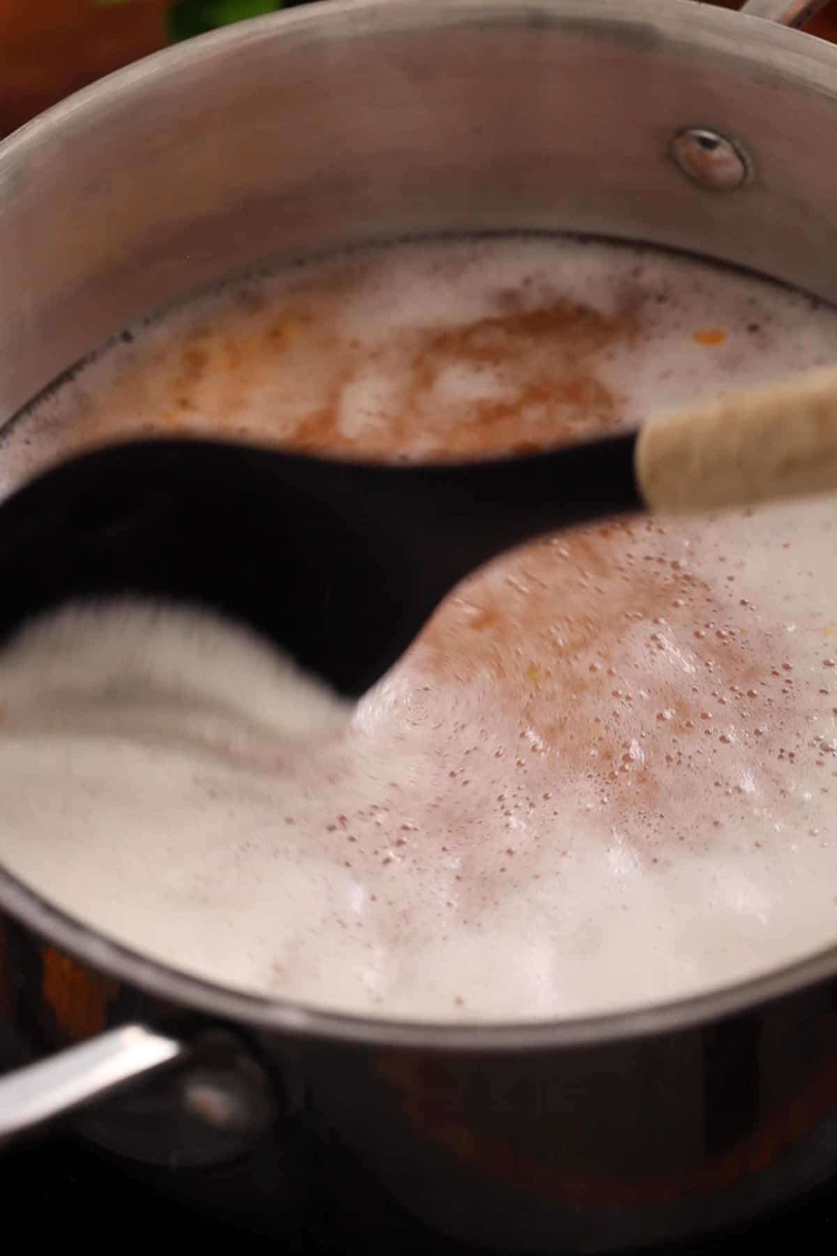 Skimming foam on top of boiling dal using a black silicone spoon.