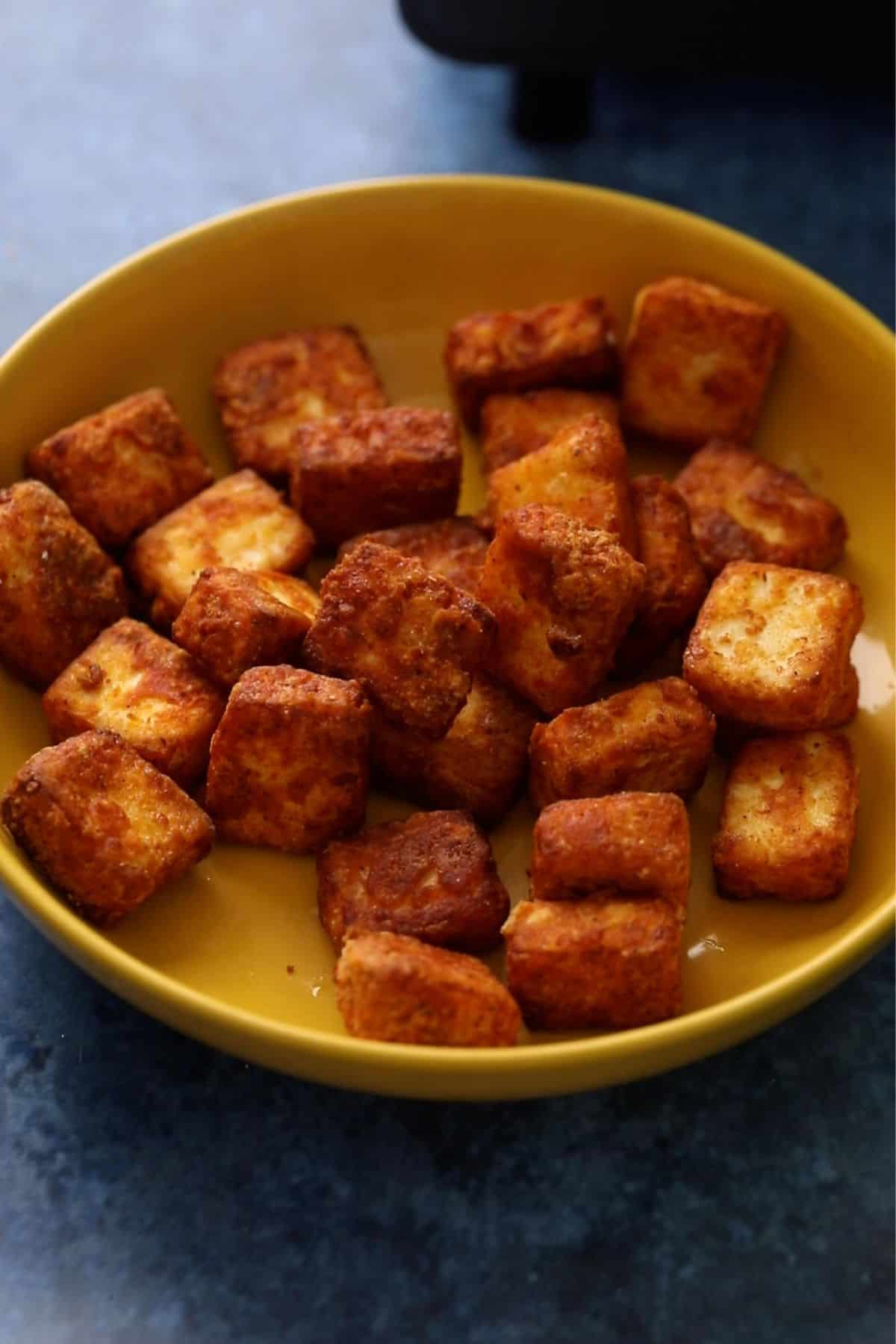 Crispy deep fried paneer pieces are placed in a shallow yellow bowl. 