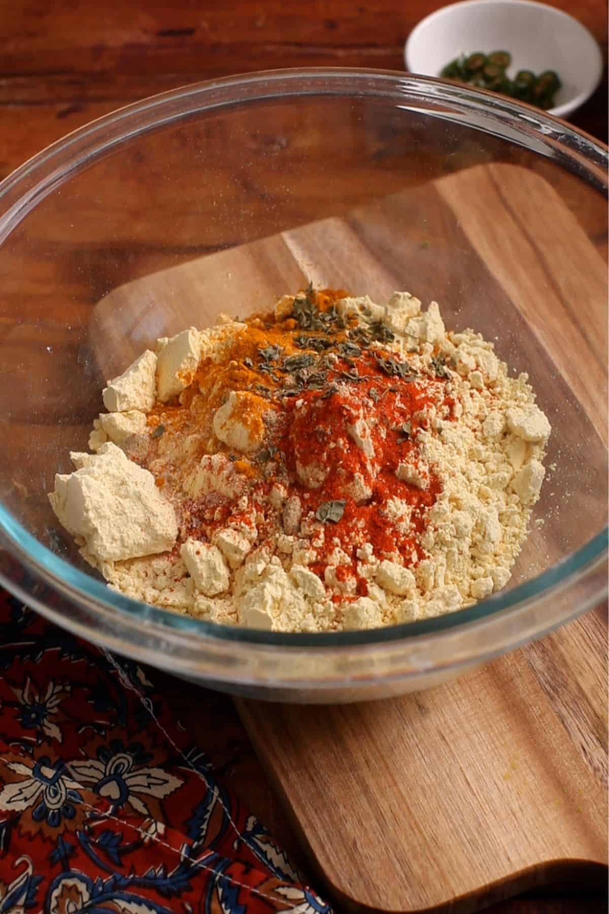 Gram flour and spices are added to a glass bowl to make fritter mix.