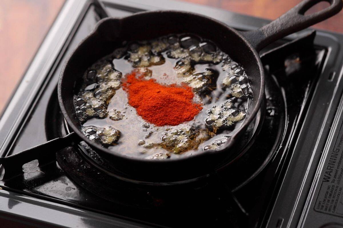 Spices are added to a small cast iron skillet to make final tadka for kadhi.