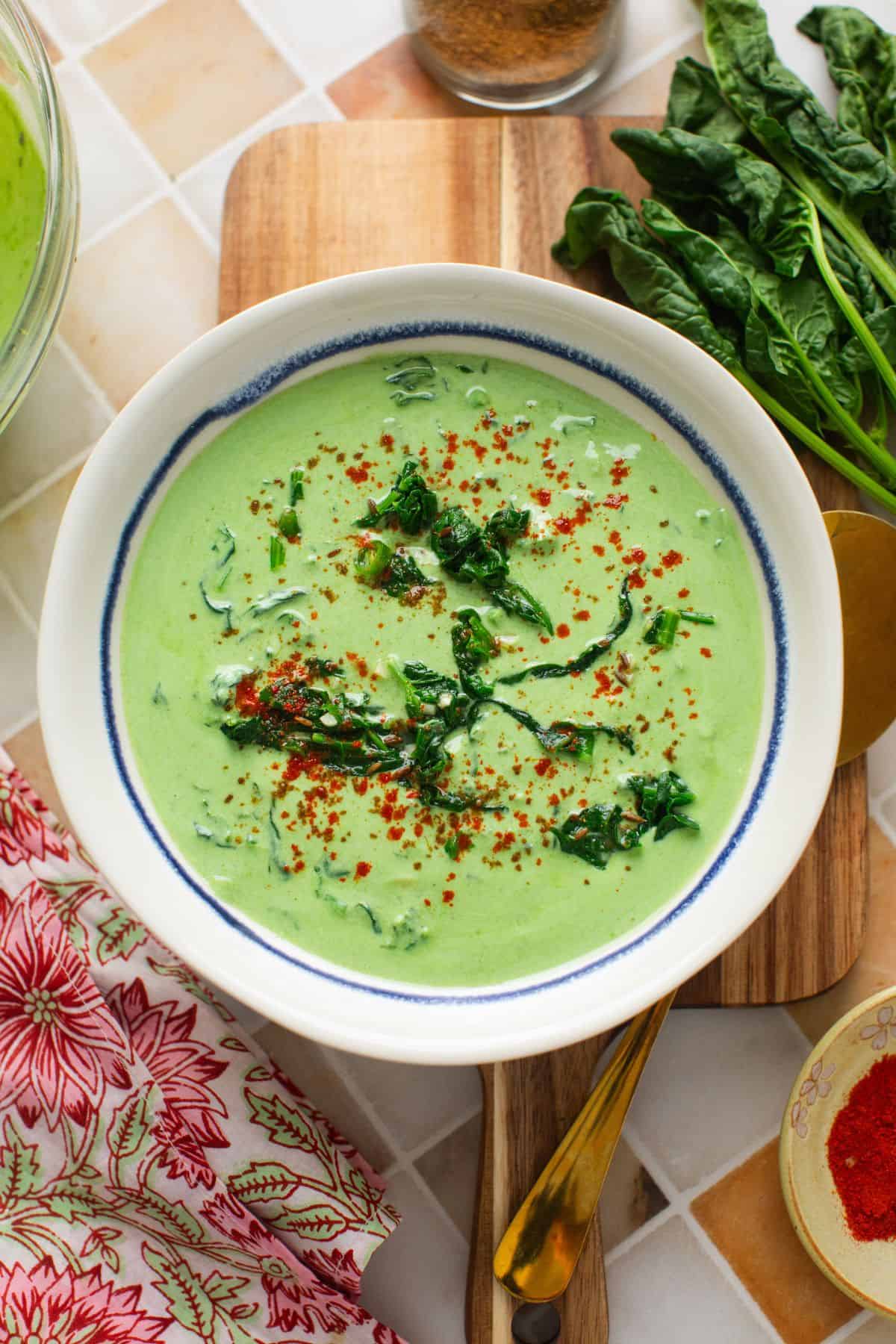 Spinach raita served in a white bowl with blue rim. 