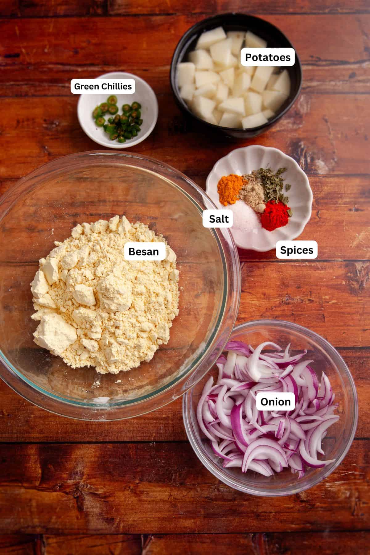 Ingredients Needed to Make potato onion pakora placed on a wood background. 