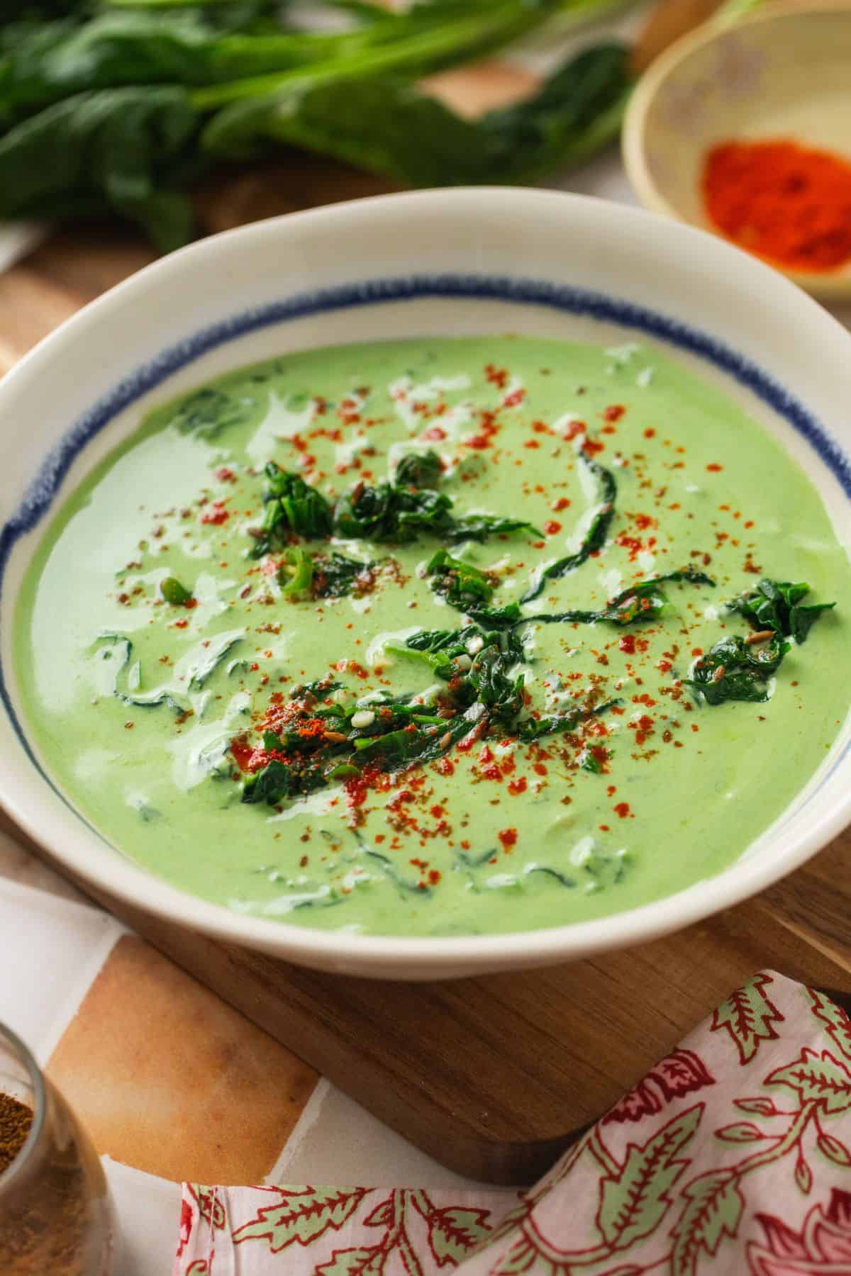 Side view of palak raita served in a white bowl with spinach leaves in background.