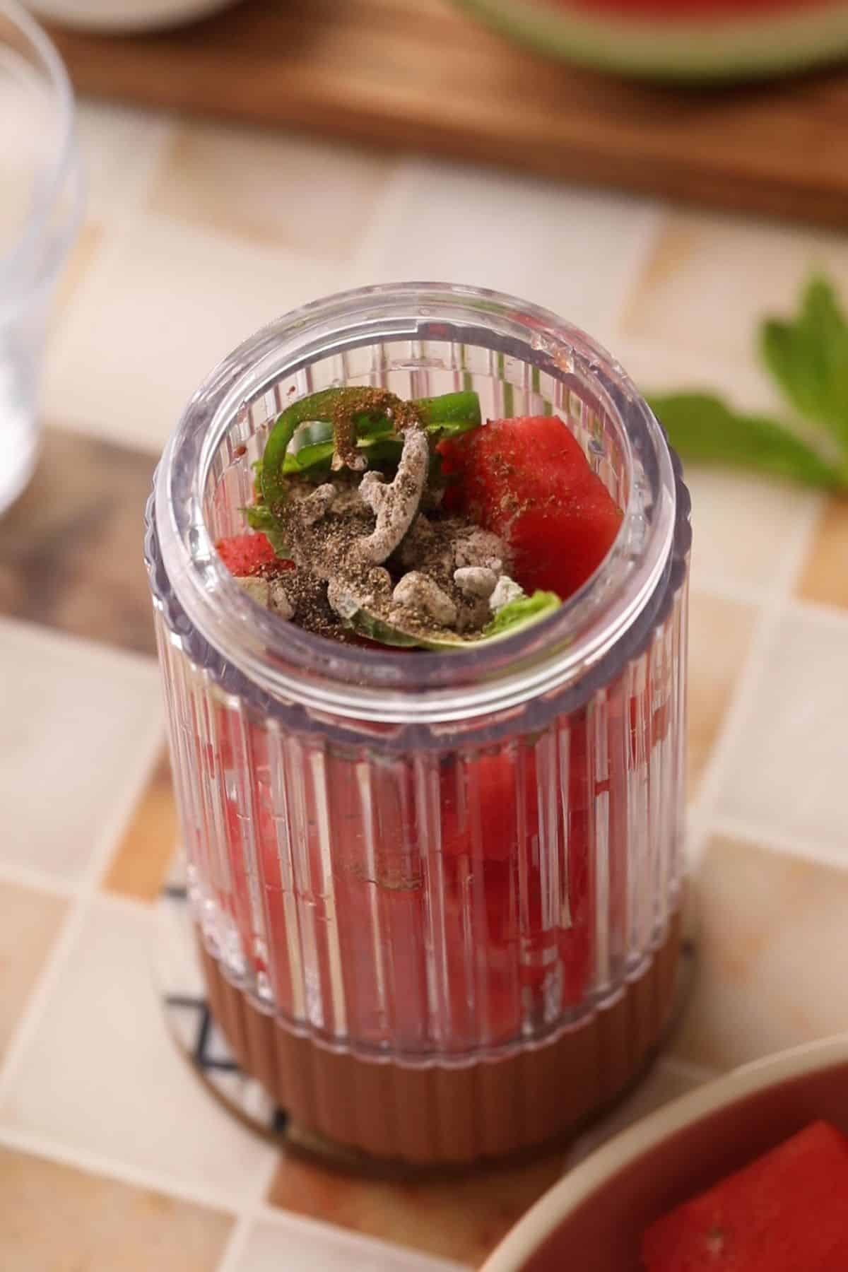 Watermelon, spices, ginger ana jalapeno are added to a coral color blender jar. 