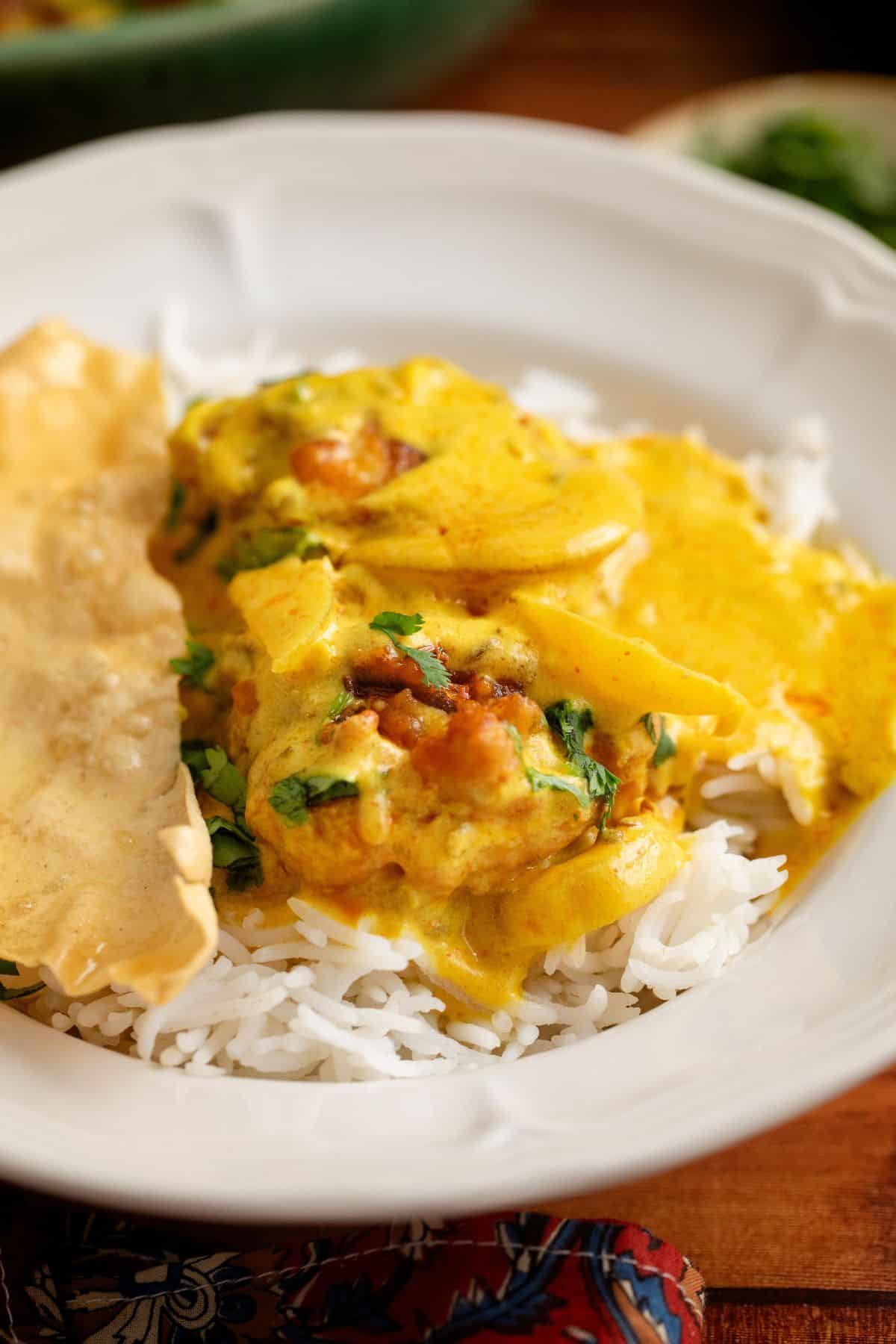 A white plate with basmati rice topped with a kadhi pakora and garnished with cilantro, served alongside a crispy papadum.