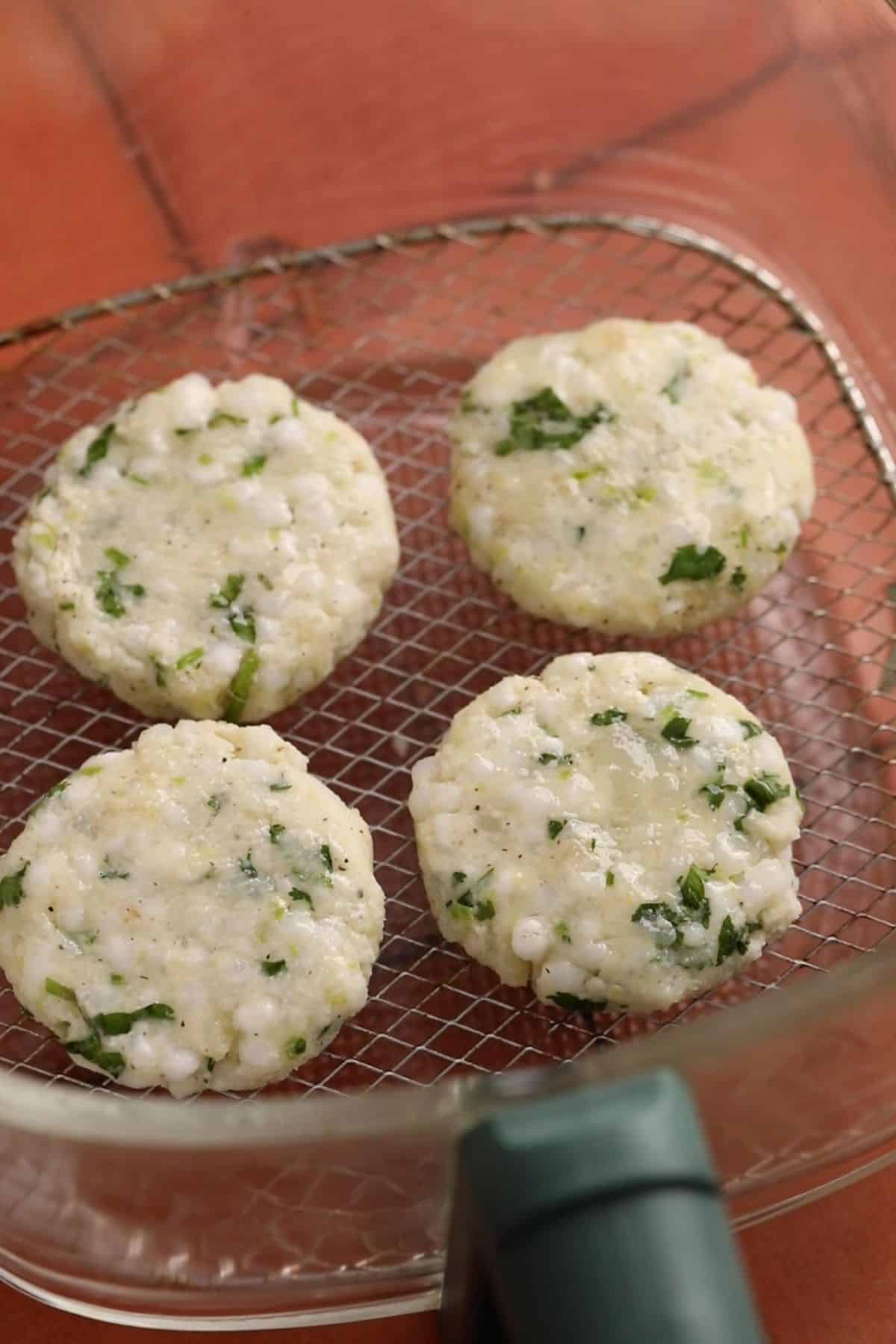 Shaped sabudana vada placed on the rack of a glass air fryer basket.