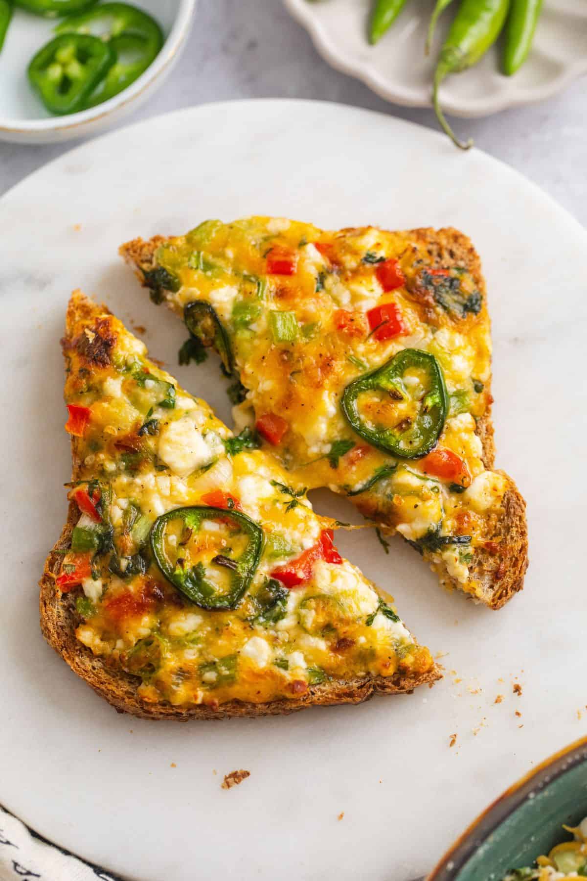 Cottage cheese chilli toast cut into half and placed on a round marble board.