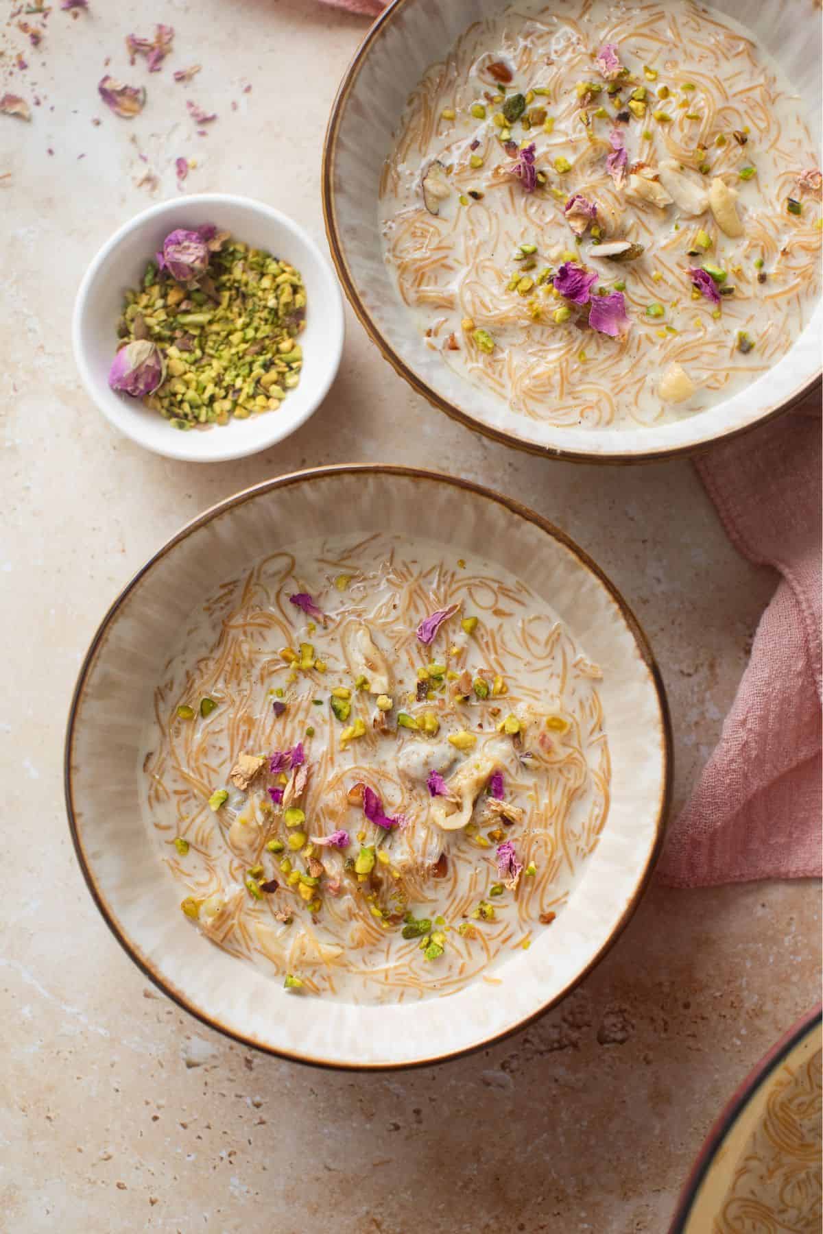 Two bowls of creamy vermicelli kheer garnished with nuts and dried rose petals.