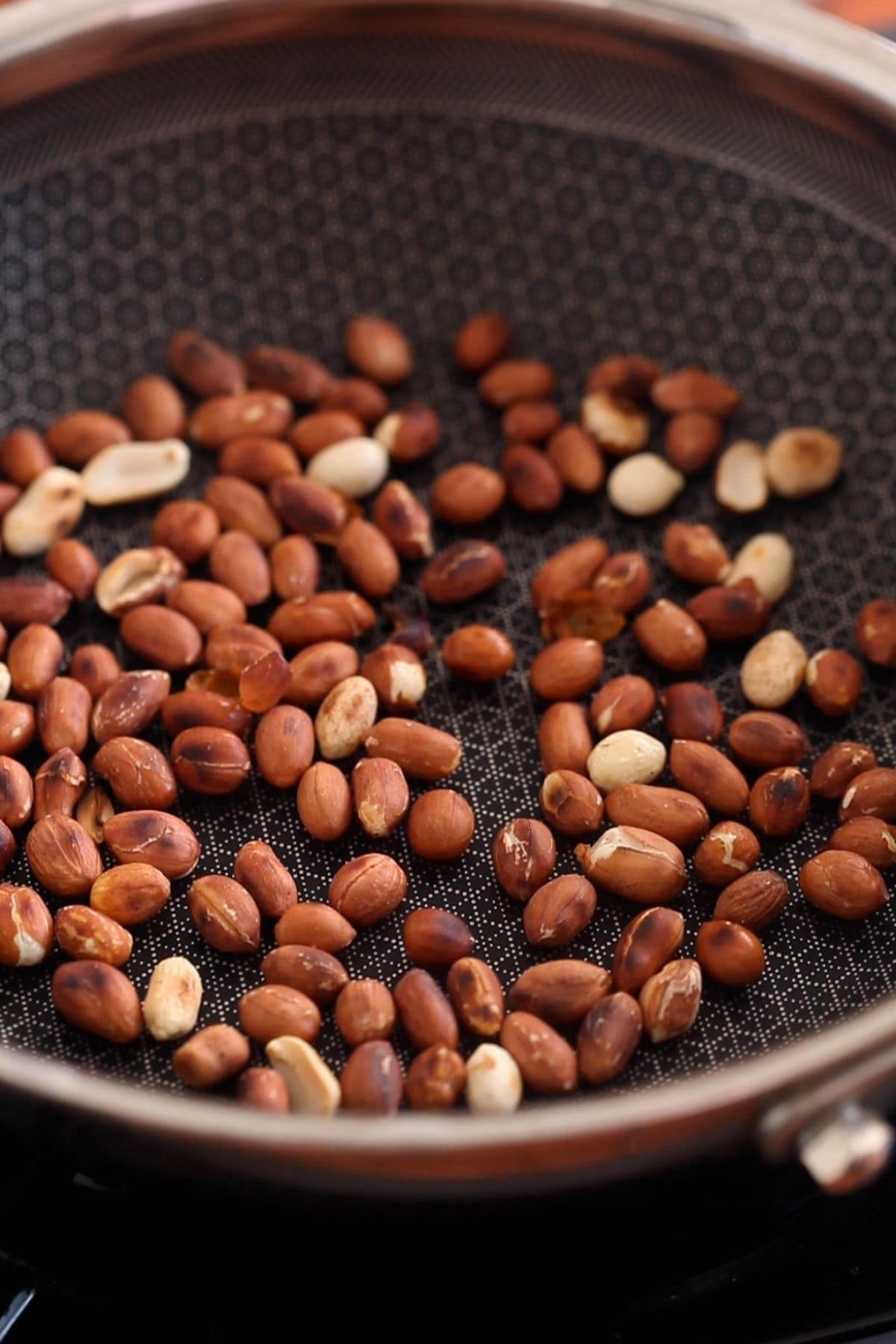 Raw peanuts are dry roasted in a black skillet.