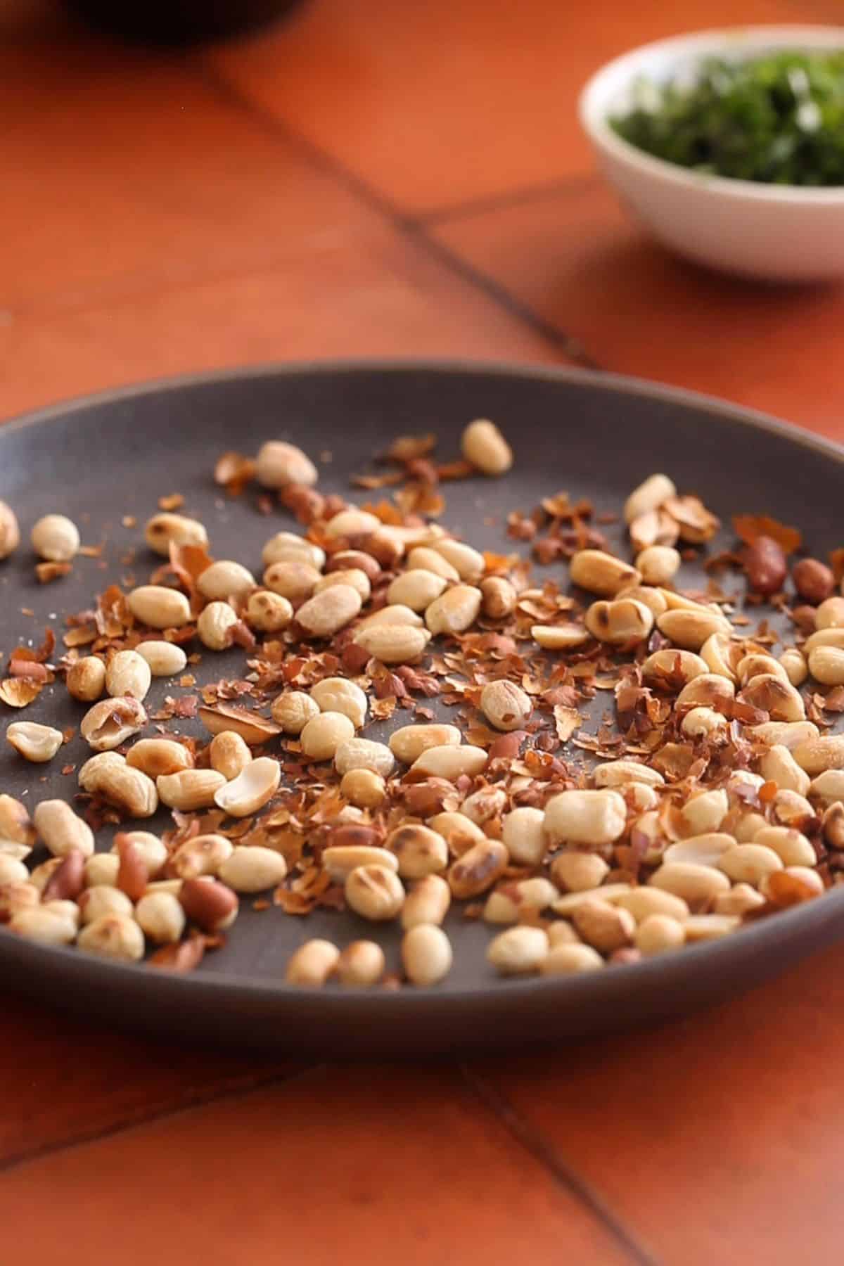 Skin is removed by rubbing from roasted peanuts placed in a dark grey plate.