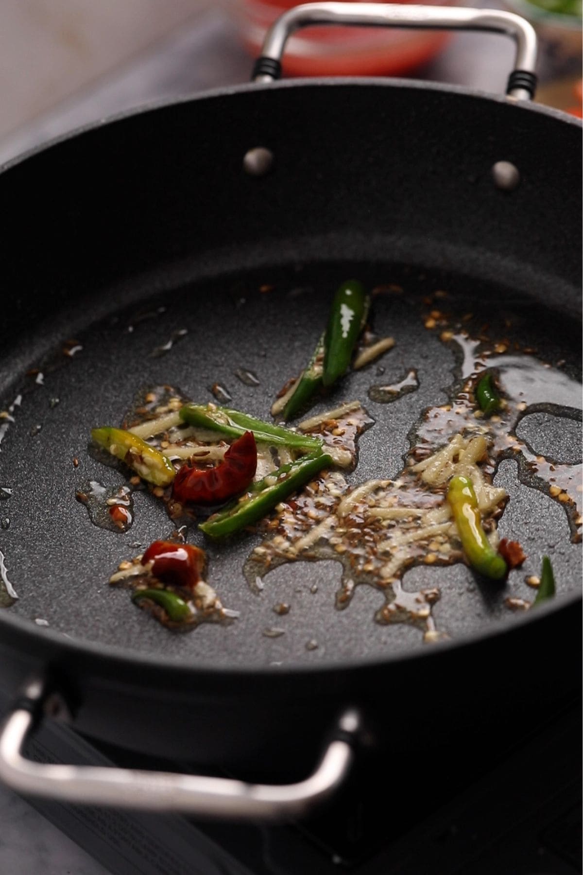 Spices, ginger and green chillies frying in oil.