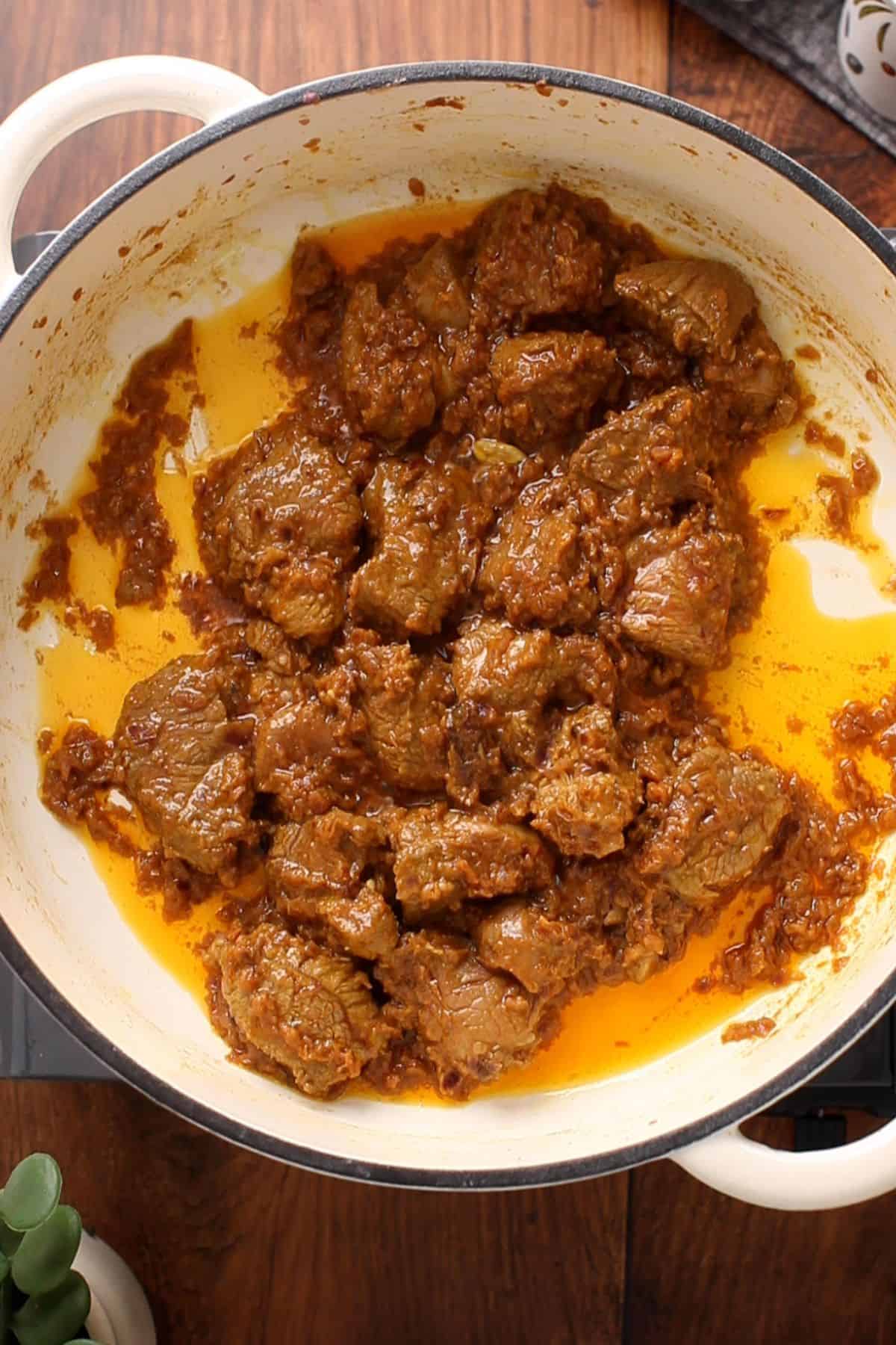 Chunks of lamb simmering in a pot with onions and oil is beginning to seperate.