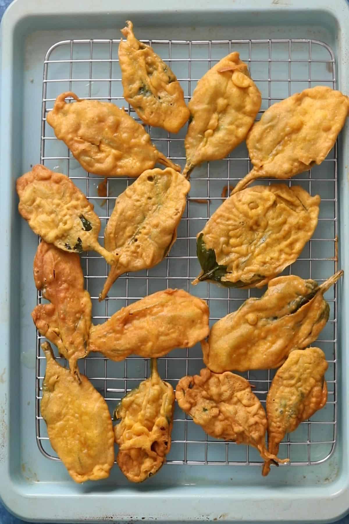 Deep fried spinach leaves are placed on a wire rack over a blue baking sheet.