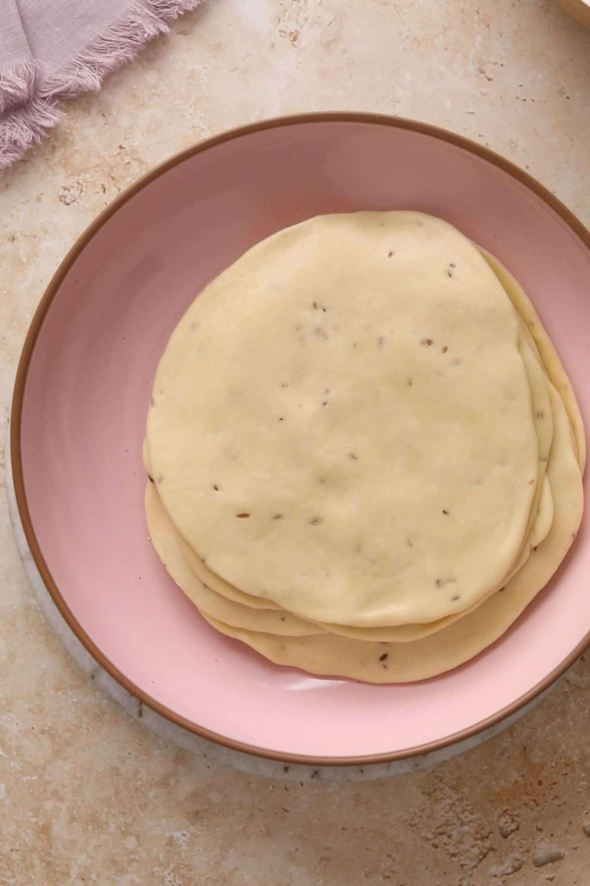 A pink bowl with all the rolled out samosa dough.