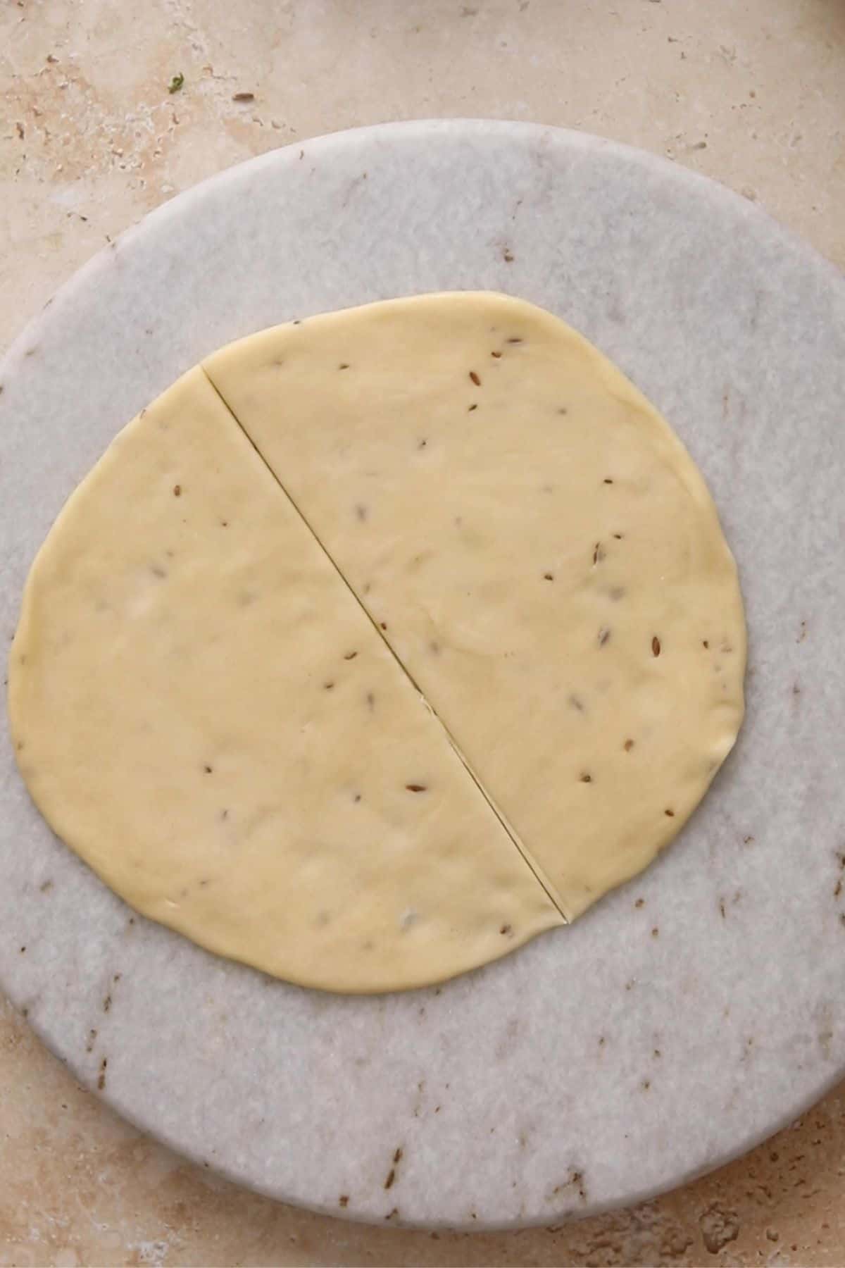 The circular dough is cut into two semi circles using a asharp knife.