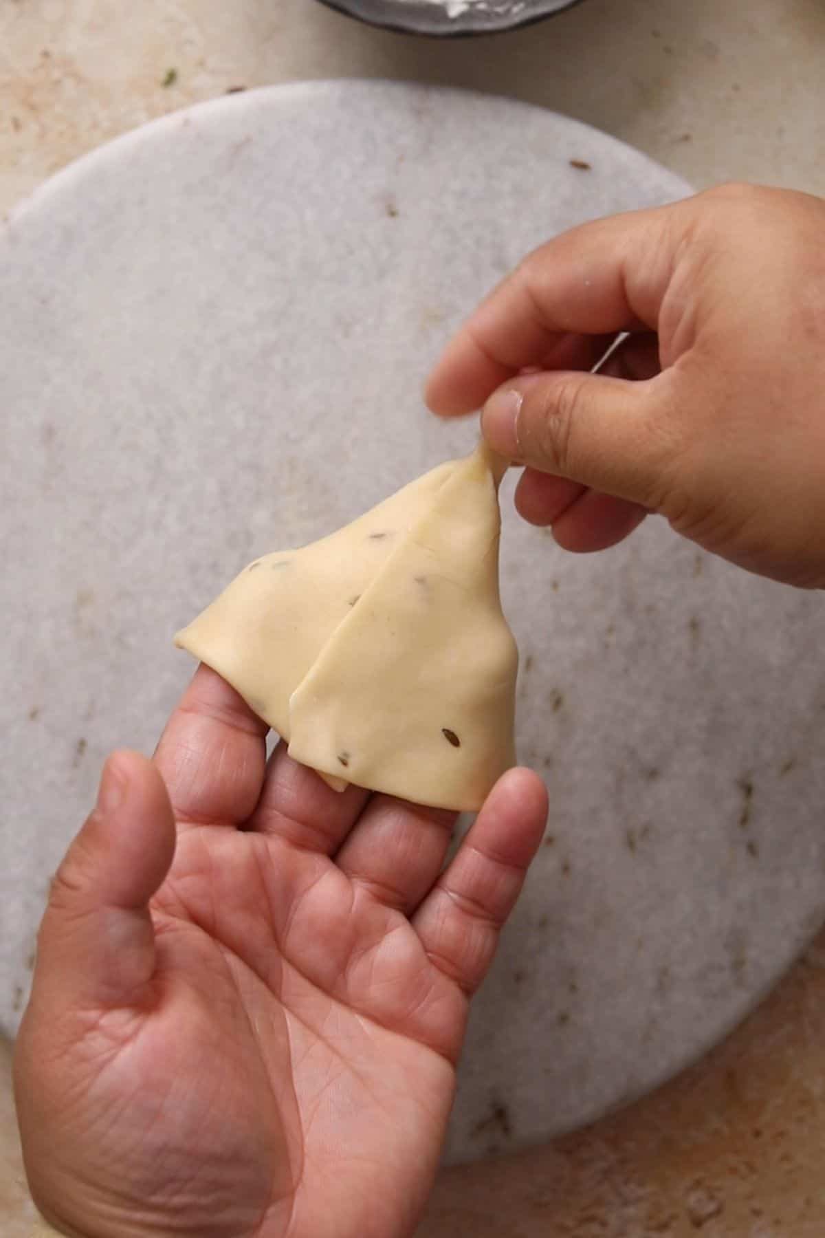 The pointed edge of samosa dough is closed to a make a pocket. 