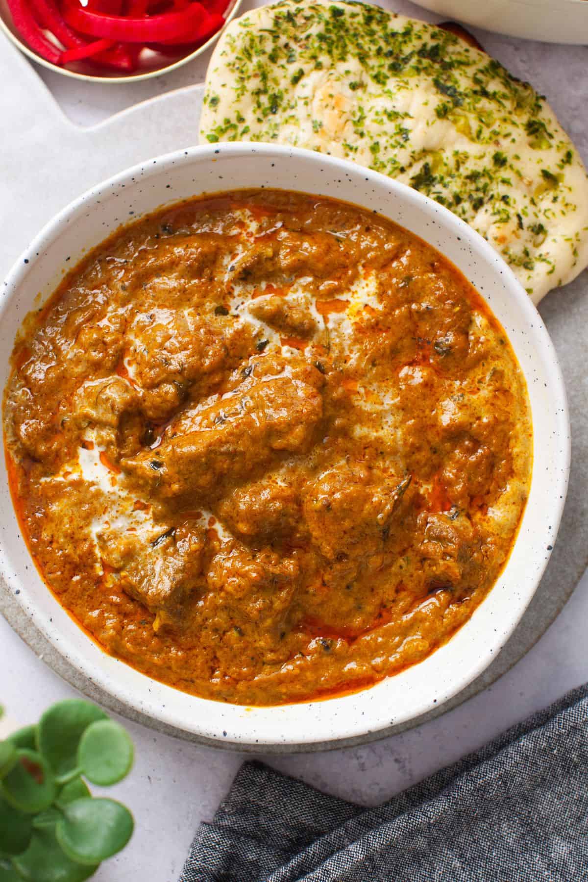 Creamy lamb korma served in a white dish with naan and pickled onions.