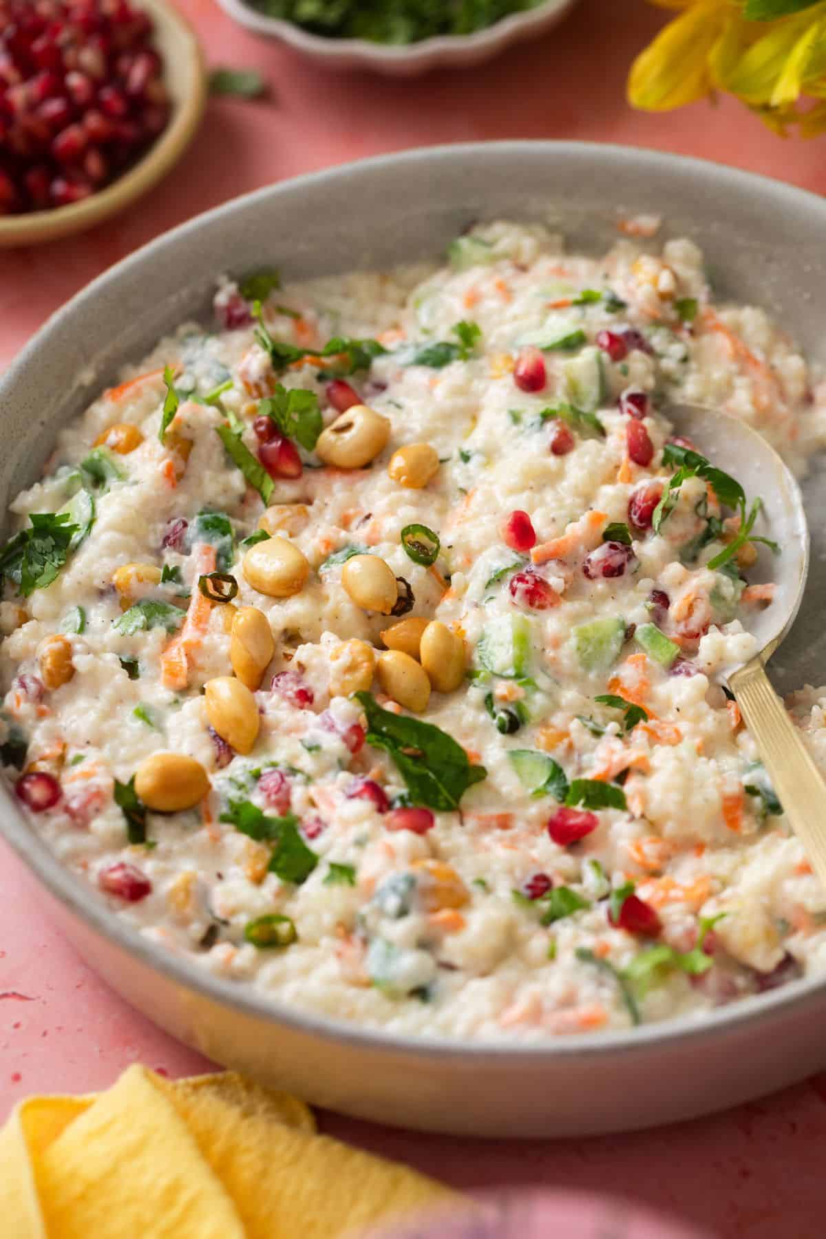 Millets Curd Rice served in a white stone shallow plate with a golden spoon.