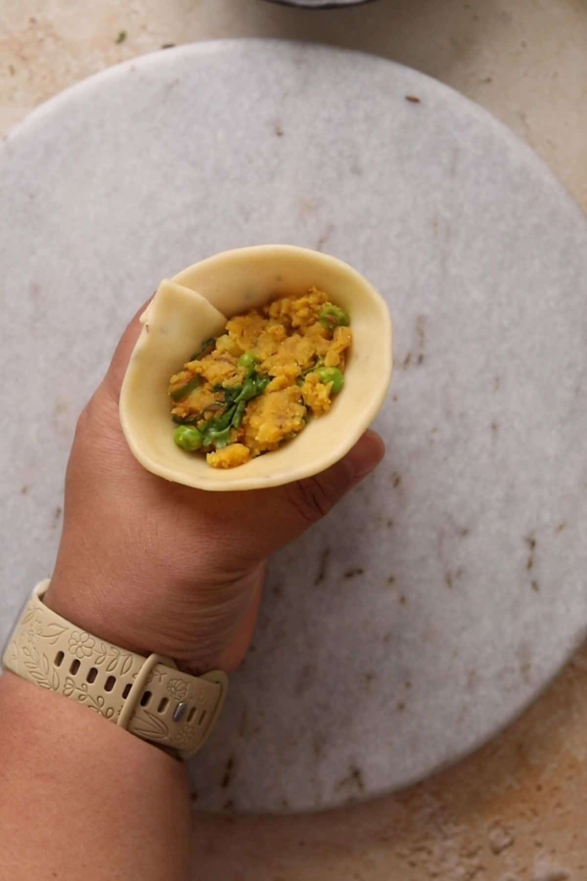 Dough pocket for samosa is filled with potato pea filling.