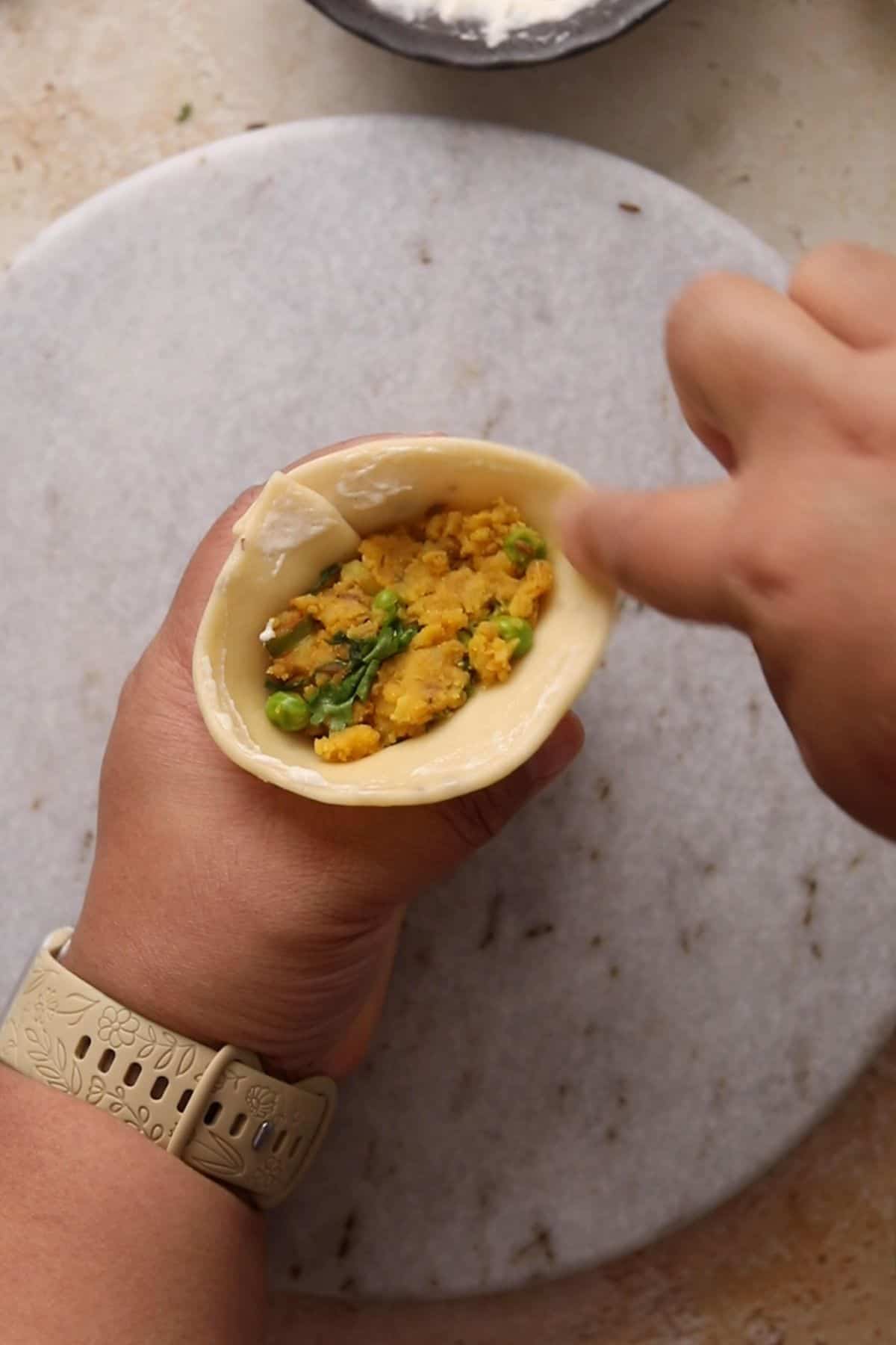 Flour slurry is applied to the edge of stuffed samosa.