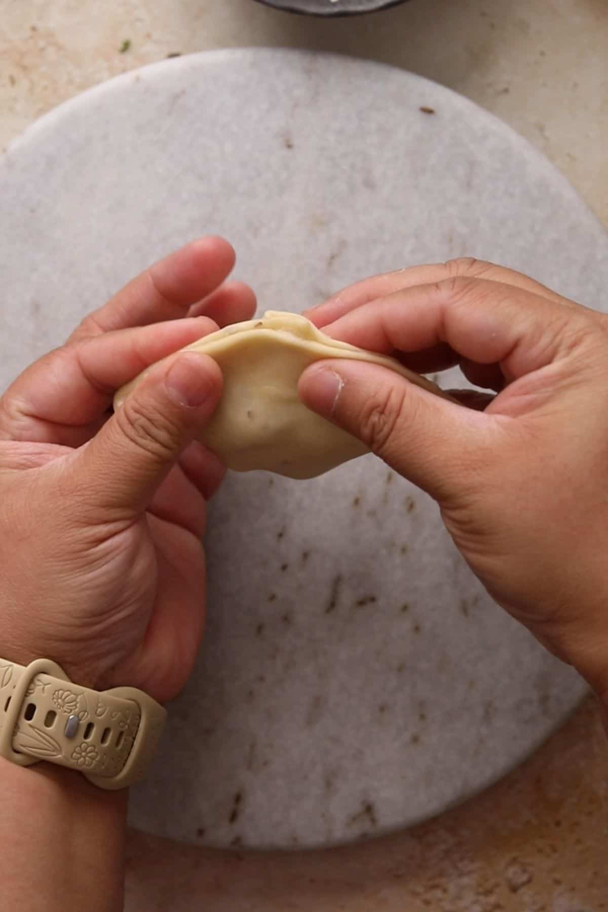 The open side of samosa dough is sealed after stuffing with potato filling.